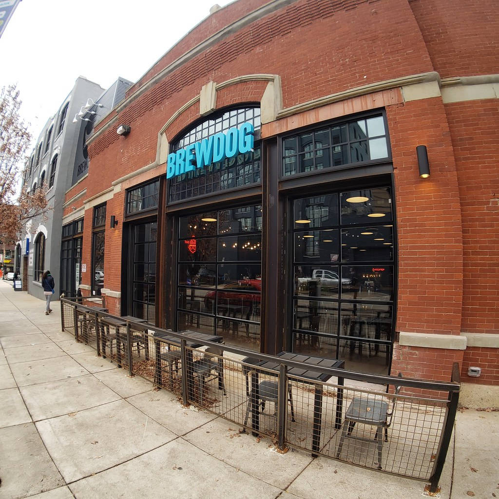 Drink 桌布 壁紙 — 紅磚 BrewDog 啤酒廠，設有大窗戶和戶外座位，位於鋪滿落葉的人行道上。