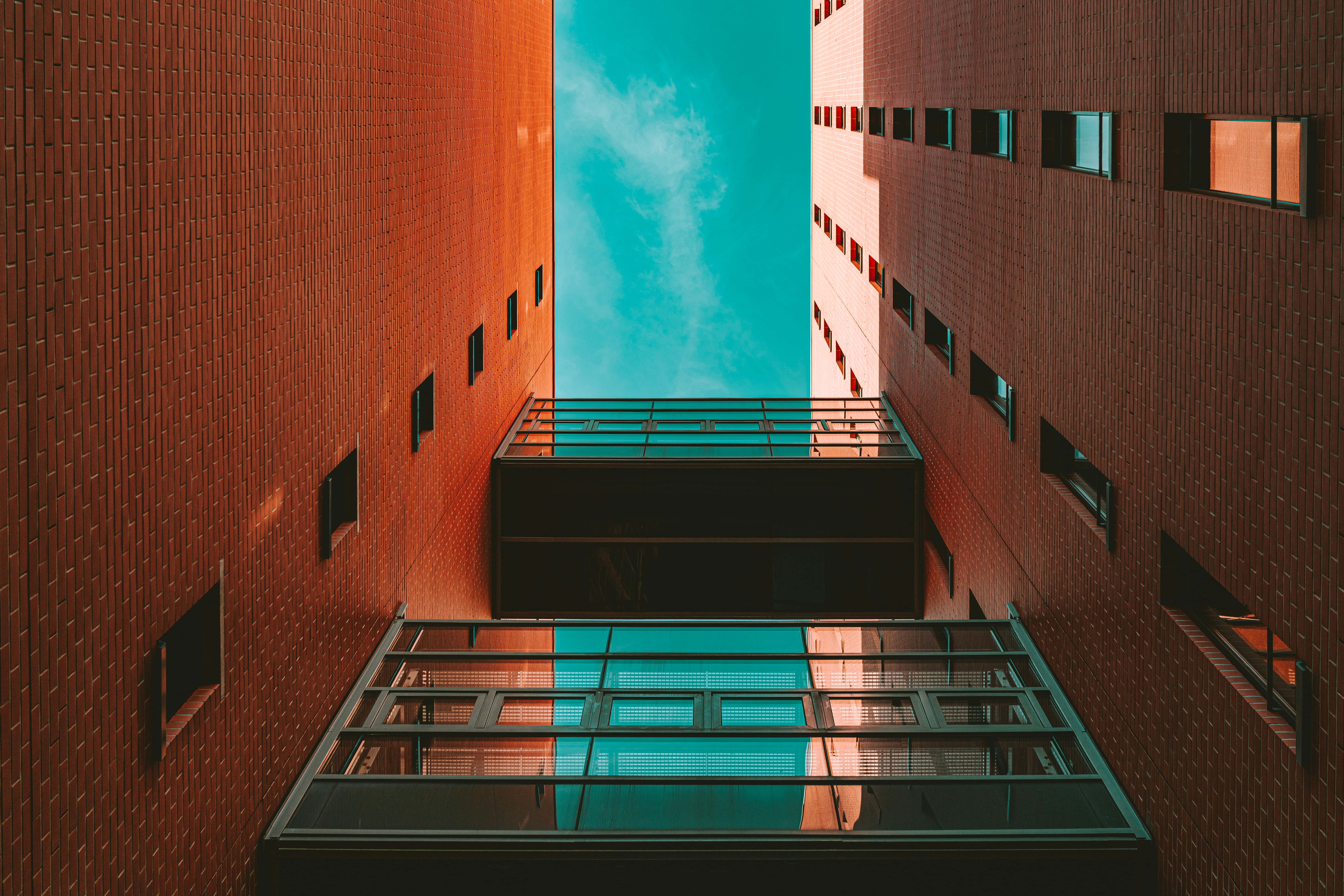 Buildings 桌布 壁紙 — 紅磚建築之間的狹窄小巷，框住了玻璃陽台上方充滿活力的綠松石色天空。