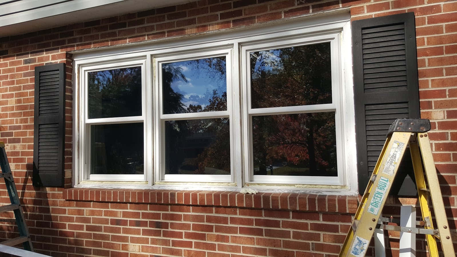 window 桌布 壁紙 — 紅磚牆上的白色三格窗搭配黑色百葉窗，在明亮日光下映照出秋天的樹木。