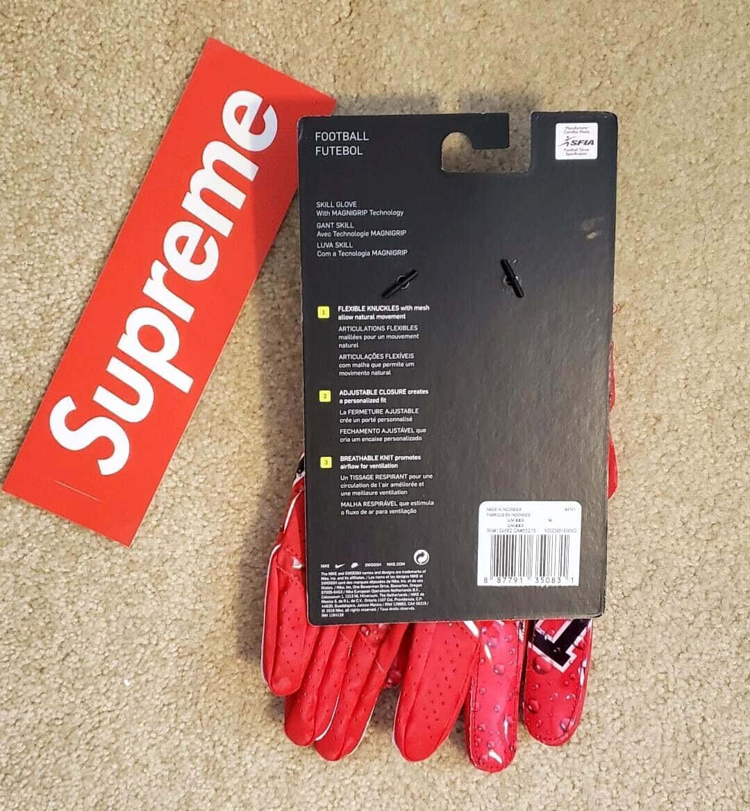 supreme 桌布 壁紙 — 紅色 Supreme 品牌美式足球手套連包裝放在米色地毯上，展示大膽標誌和產品細節。