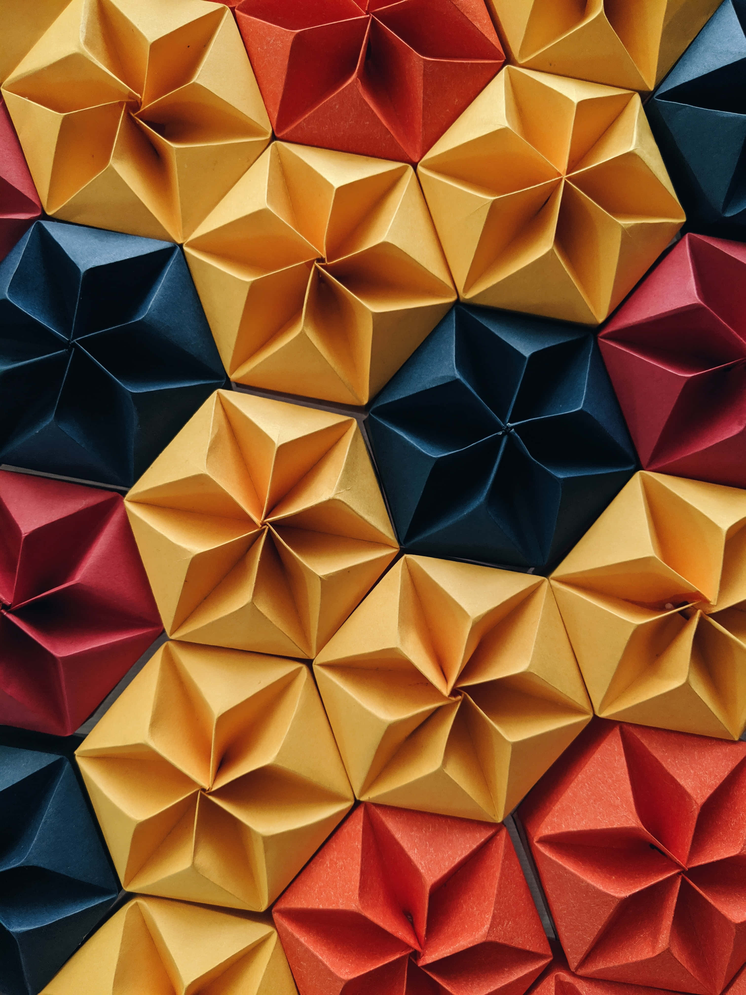 3D 桌布 壁紙 — 紅色、金色和深藍色的鮮豔幾何摺紙星星以重複圖案排列的特寫。