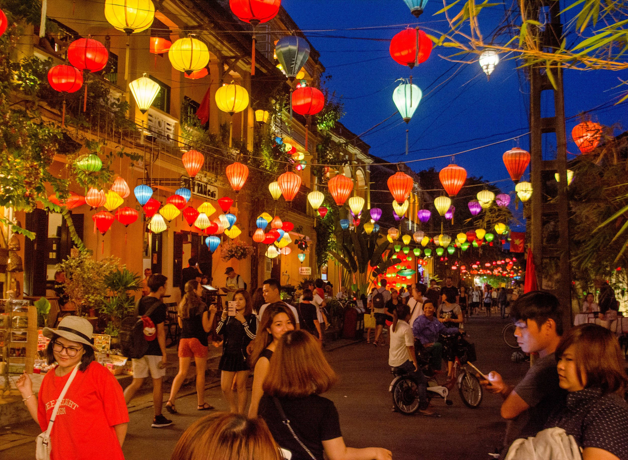 Hanoi 桌布 壁紙 — 紅色、黃色和藍色的鮮豔燈籠在黃昏時分照亮了一條擠滿人的繁華街道。