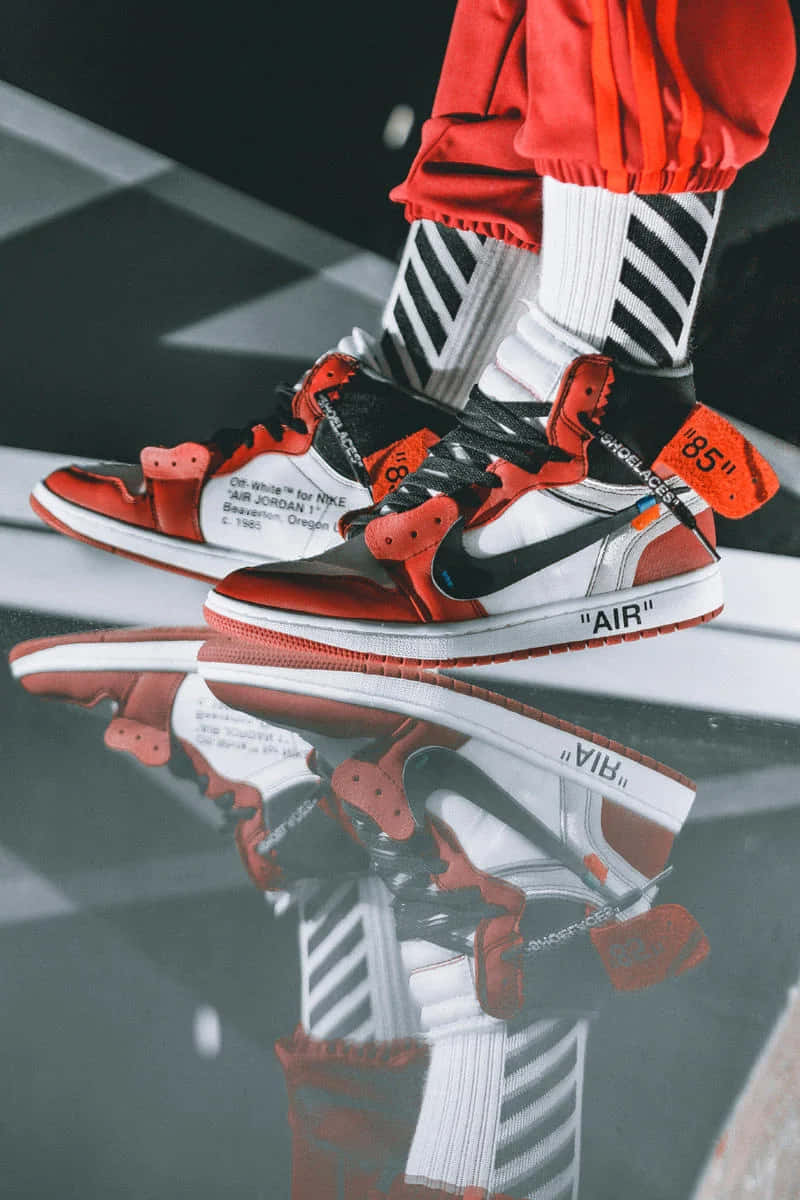 潮流玩家 桌布 壁紙 — 紅色、黑色和白色 Off-White x Nike Air Jordan 1 運動鞋與條紋襪子在光澤地板上的特寫反射。