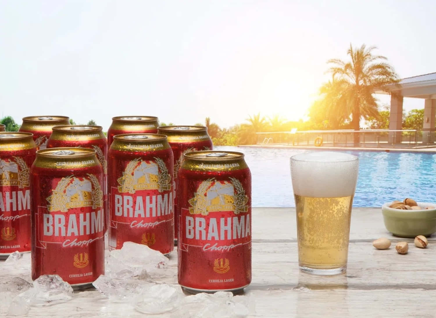 Drink 桌布 壁紙 — 紅色Brahma啤酒罐和一個有泡沫的玻璃杯放在泳池邊的冰上，背景是金色日落和棕櫚樹。