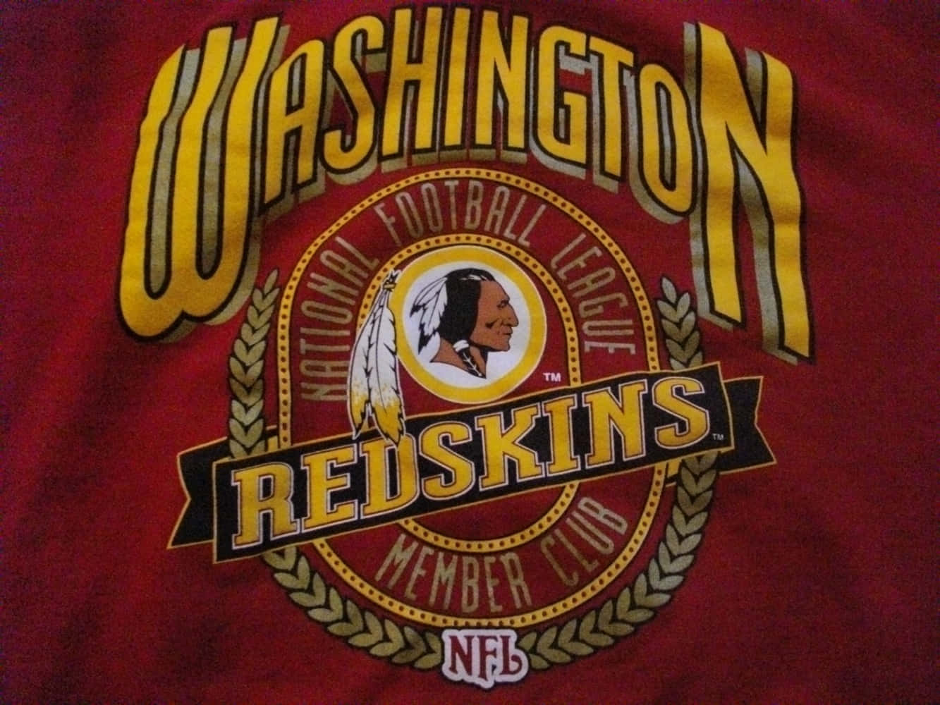 Washington Football 桌布 壁紙 — 紅色T恤近距離特寫，上面有華盛頓紅皮隊NFL標誌，採用黃色和金色文字，以及美洲原住民側面輪廓徽章。