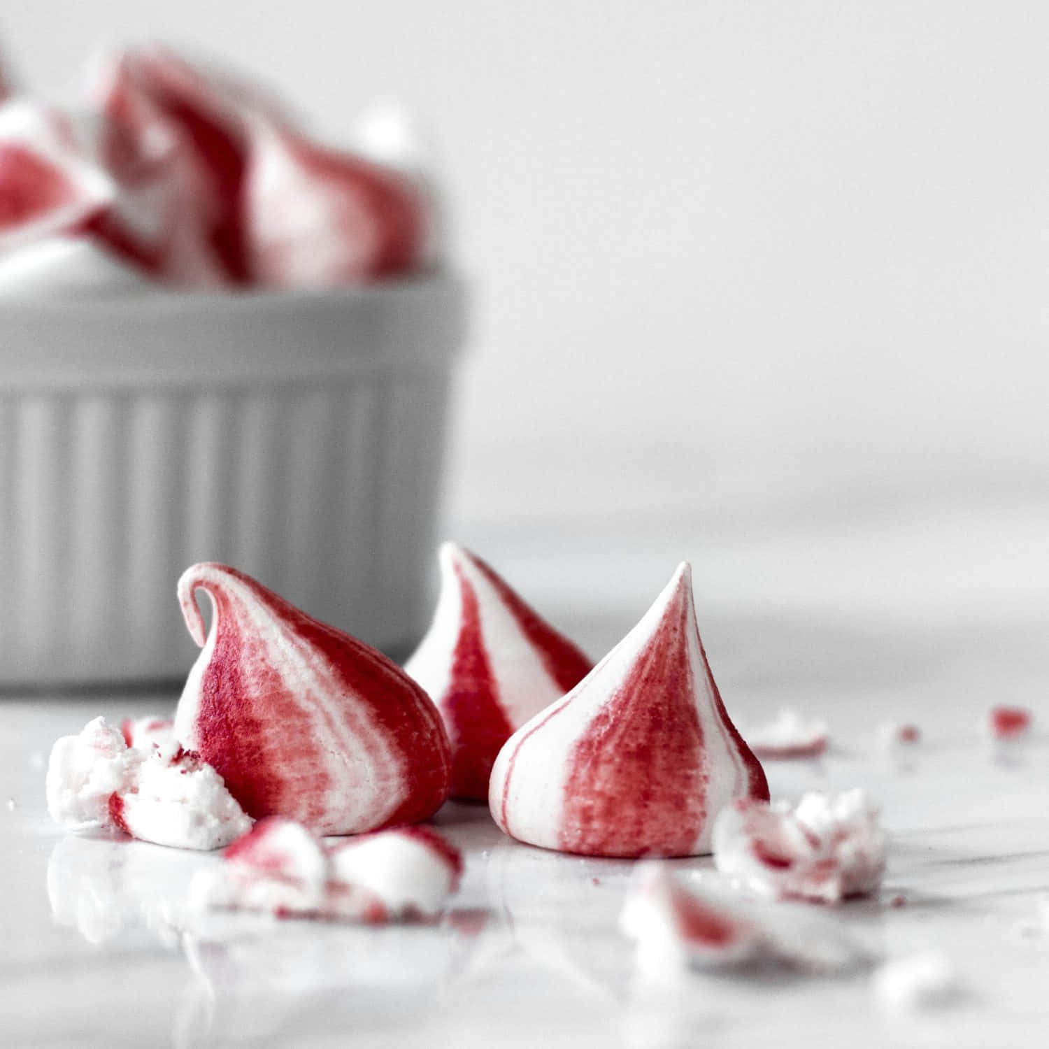 Meringue 桌布 壁紙 — 紅色和白色漩渦狀的蛋白霜之吻放在大理石表面上，背景有一個模糊的碗。