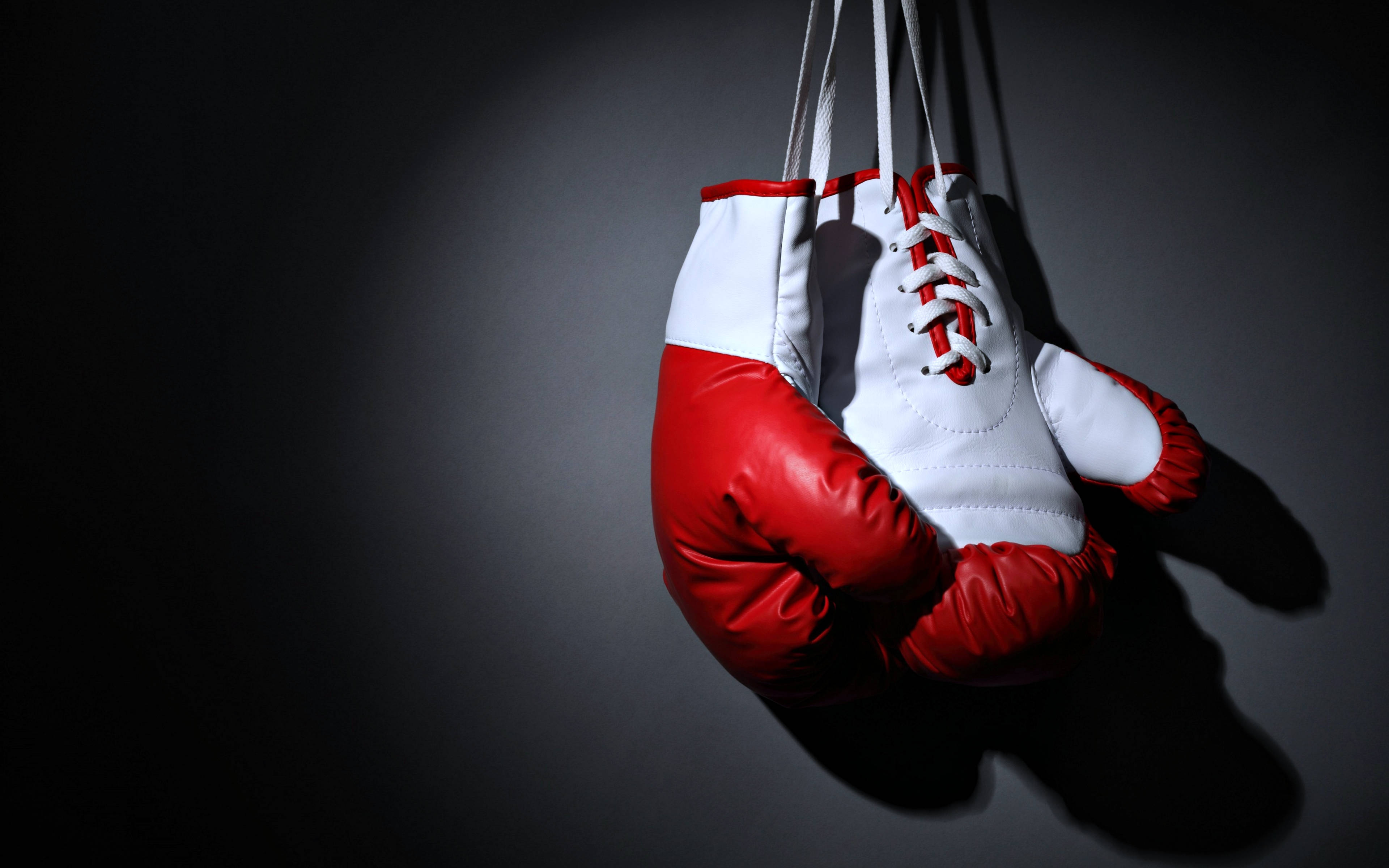Boxing 桌布 壁紙 — 紅色和白色的拳擊手套懸掛在深灰色背景上，在戲劇性的聚光燈下。