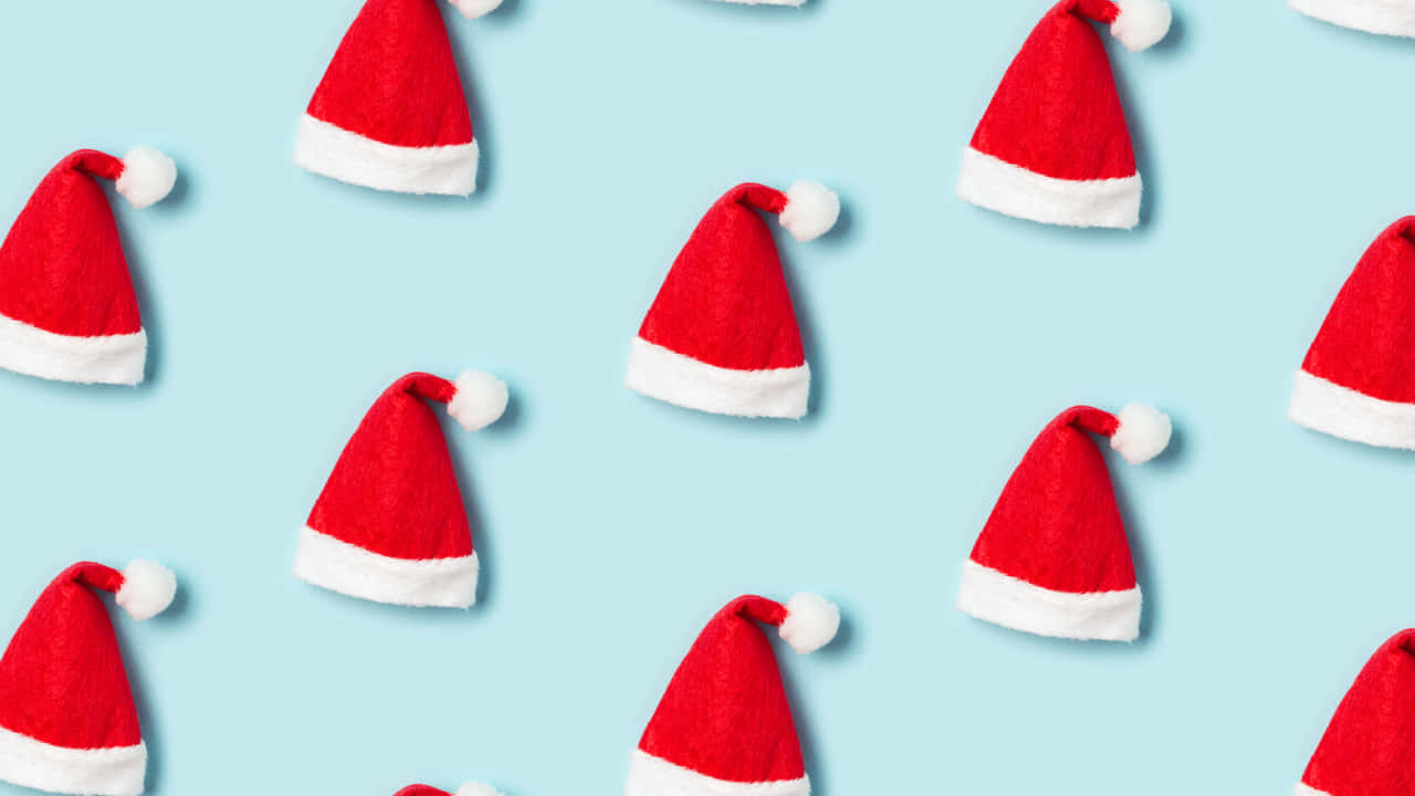 Christmas Hat 桌布 壁紙 — 紅色和白色的聖誕帽散落在柔和的藍色背景上，形成俏皮的重複圖案。