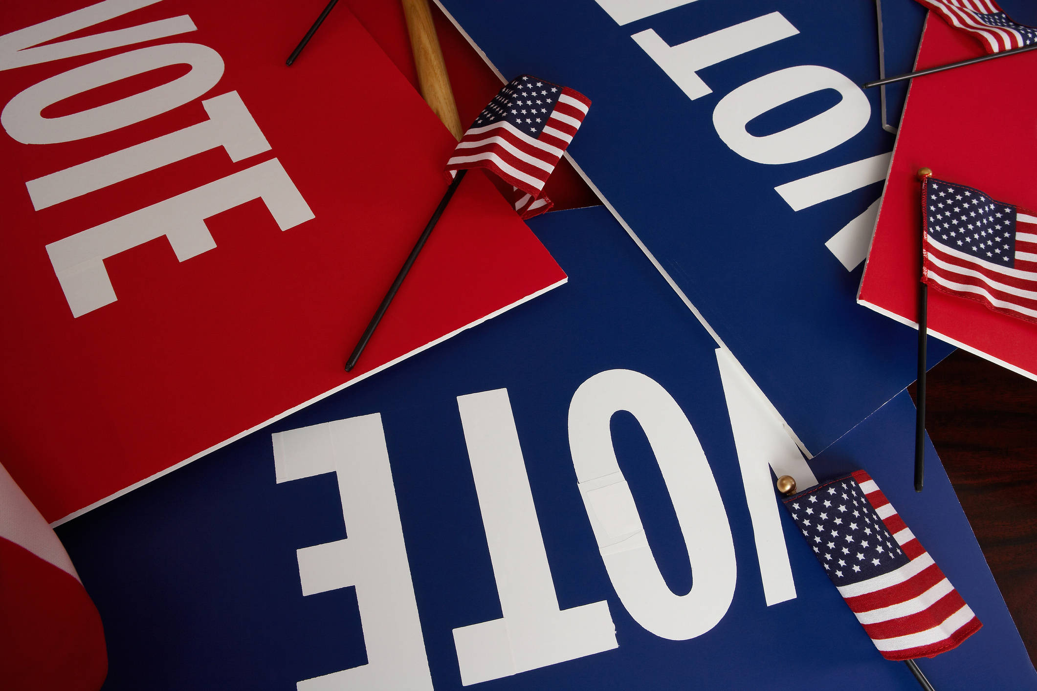 Election 桌布 壁紙 — 紅色和藍色的「VOTE」標誌，搭配微型美國國旗，以動態俯視構圖排列。