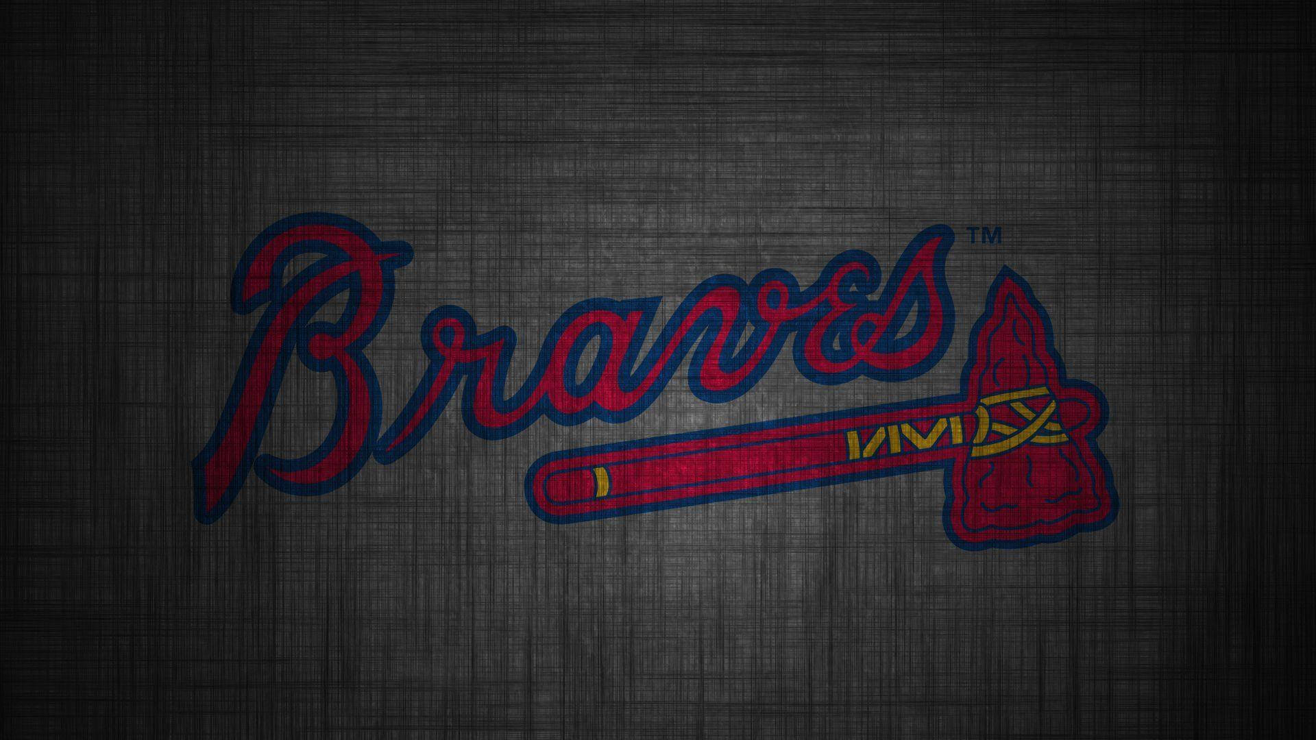 Braves 桌布 壁紙 — 紅色和藍色的亞特蘭大勇士隊標誌，帶有戰斧徽章，位於紋理深灰色織物背景上。