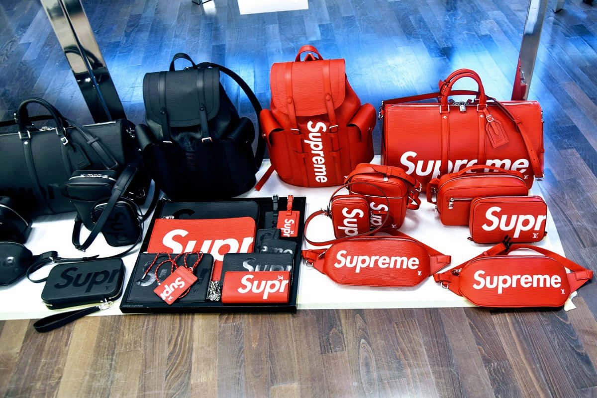supreme 桌布 壁紙 — 紅色和黑色的 Supreme 品牌手提包和配件整齊地排列在木地板上的白色表面上的鮮豔展示。