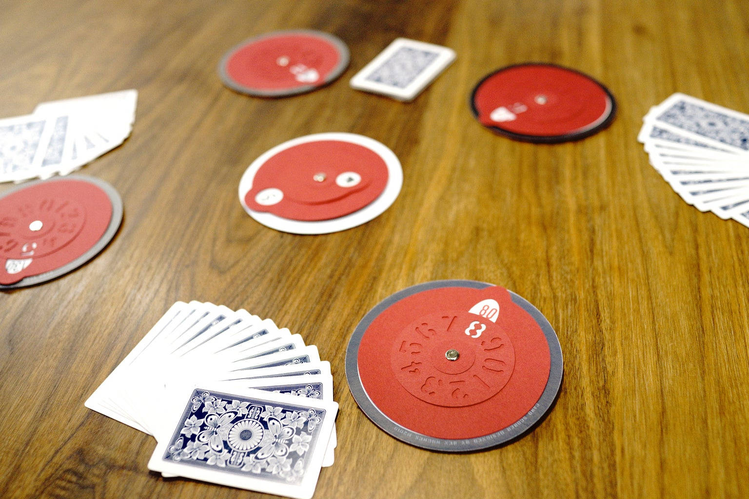 Playing Cards 桌布 壁紙 — 紅色圓形遊戲籌碼和扇形散開的撲克牌散落在溫暖的木桌面上。