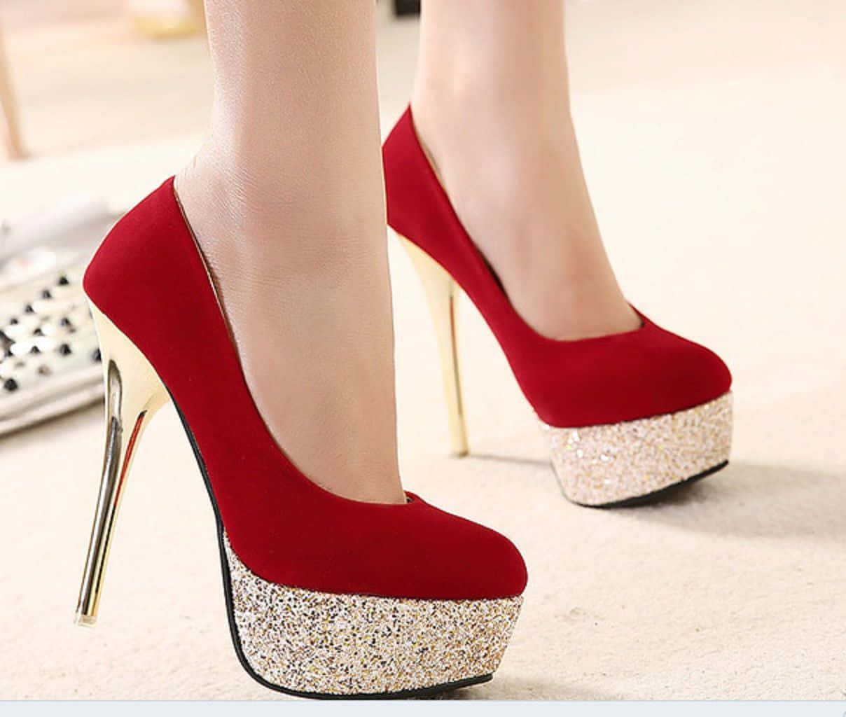 Red High Heels 桌布 壁紙 — 紅色天鵝絨厚底高跟鞋，搭配金色細高跟和閃亮鞋底，由一位站在淺色地板上的人穿著。