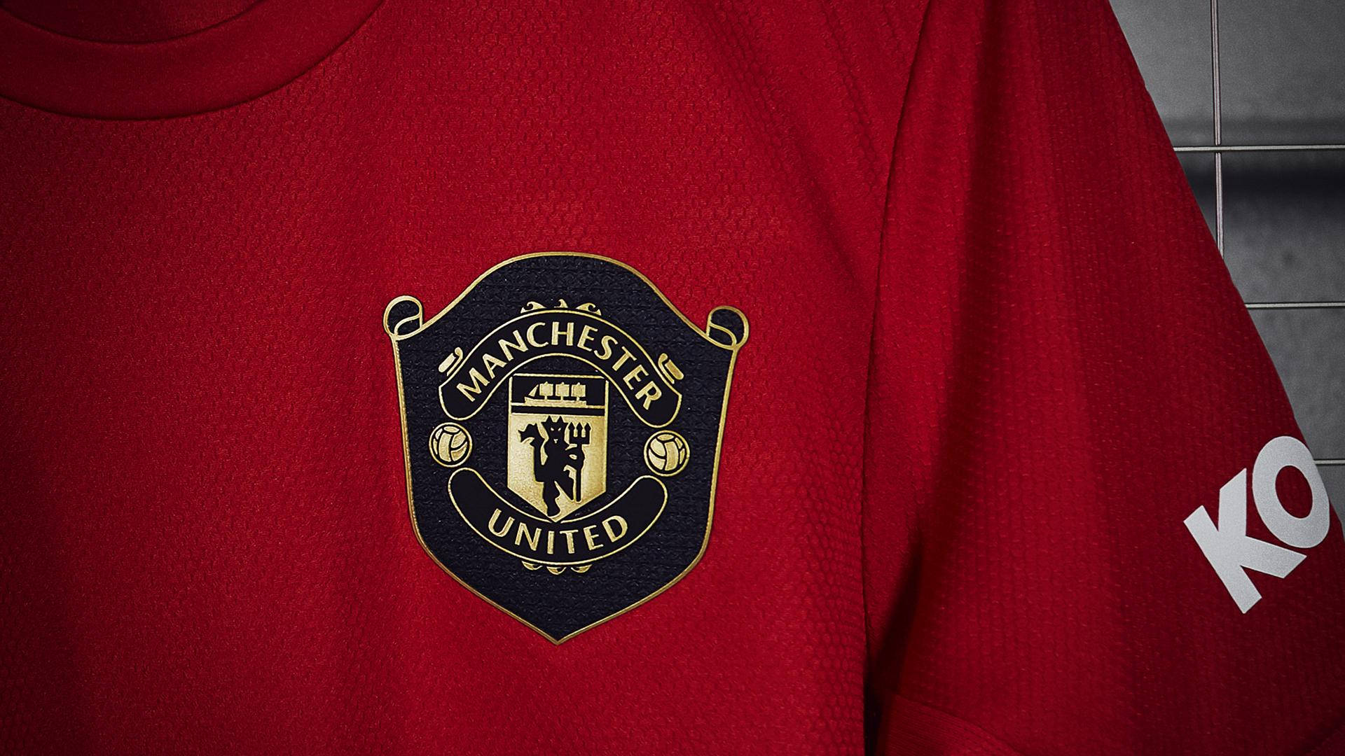 Manchester United Logo 桌布 壁紙 — 紅色曼聯足球球衣近距離特寫，帶有刺繡會徽和贊助商標誌，背景為瓷磚牆。