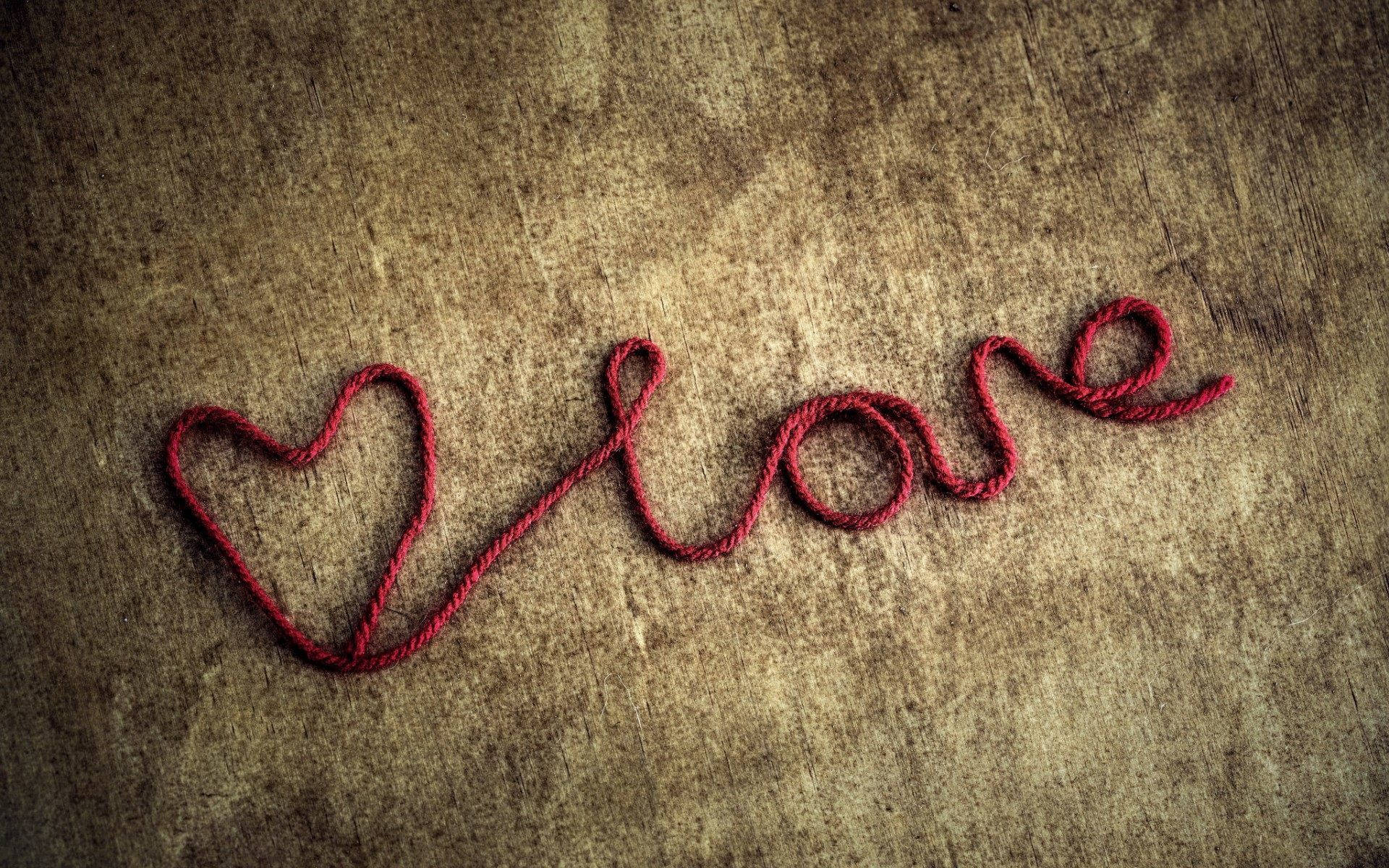 愛心 桌布 壁紙 — 紅色毛線在質感棕色表面上拼出帶有心形的love。