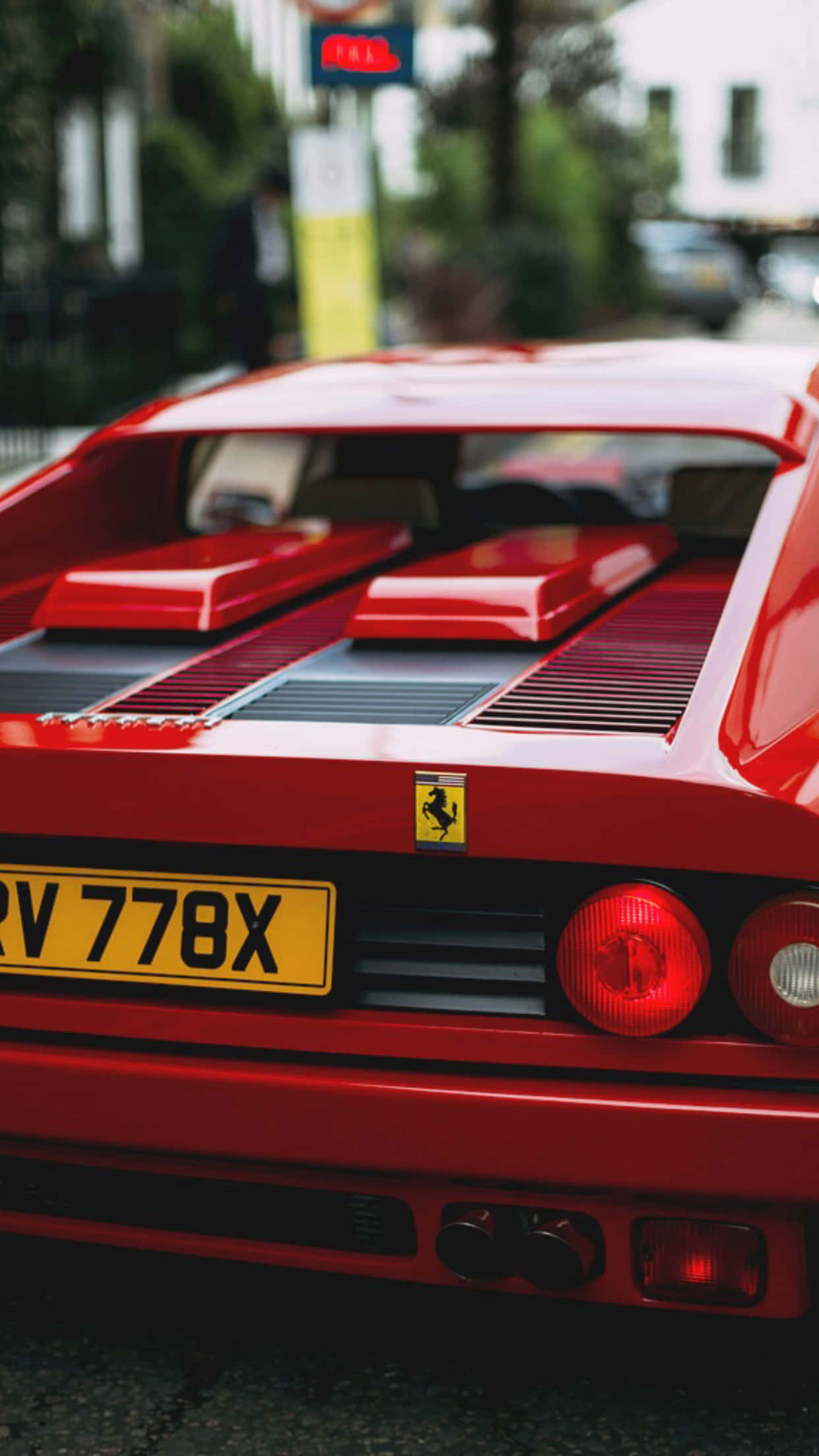 Vintage Ferrari 桌布 壁紙 — 紅色法拉利F40車尾特寫，展示其標誌性通風口和發光尾燈，背景為模糊的城市景觀。
