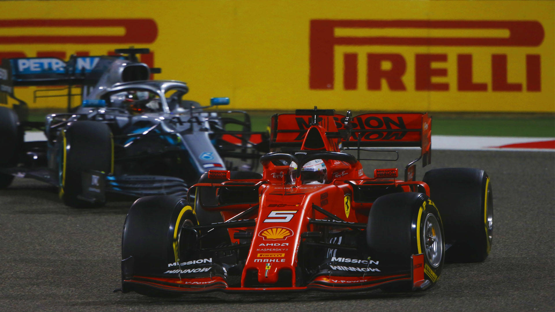 Formula 1 2019 桌布 壁紙 — 紅色法拉利一級方程式賽車，車號5，在明亮燈光下緊跟在藍色賓士賽車後方，在濕滑賽道上競速。