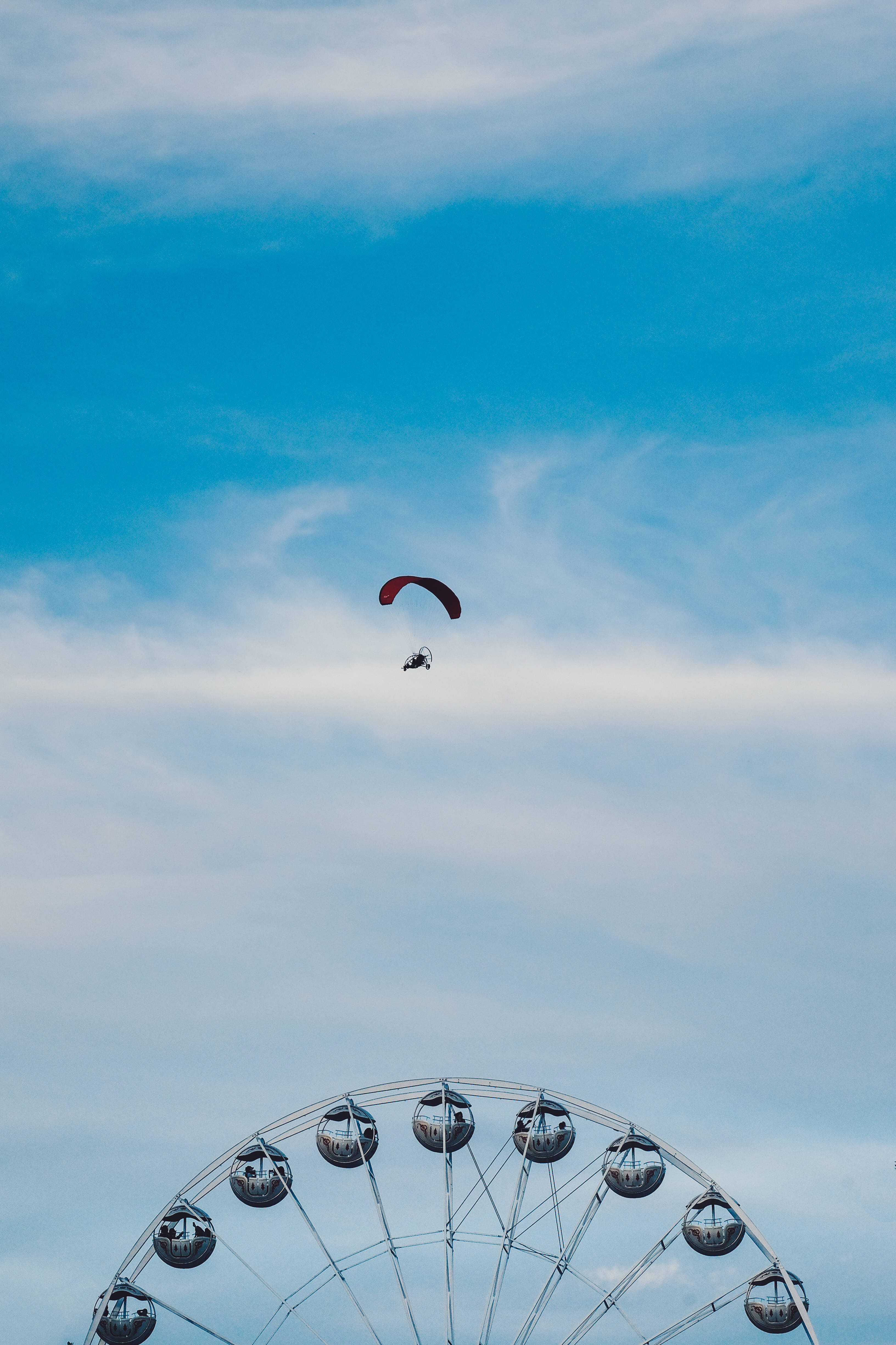 Paragliding 桌布 壁紙 — 紅色滑翔傘在明亮的藍天和薄雲下翱翔於大型摩天輪之上。