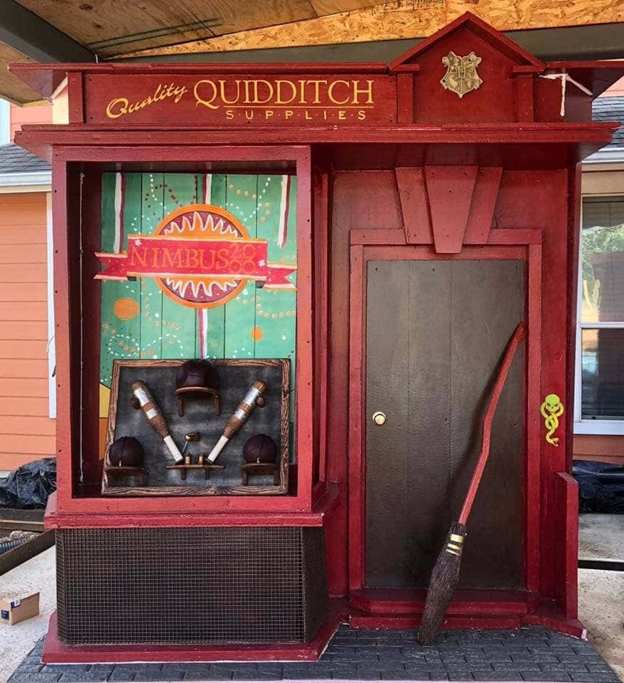 Diagon Alley 桌布 壁紙 — 紅色的 Quidditch Supplies 店面在綠色圖案窗戶下方展示 Nimbus 2000 掃帚和裝備。