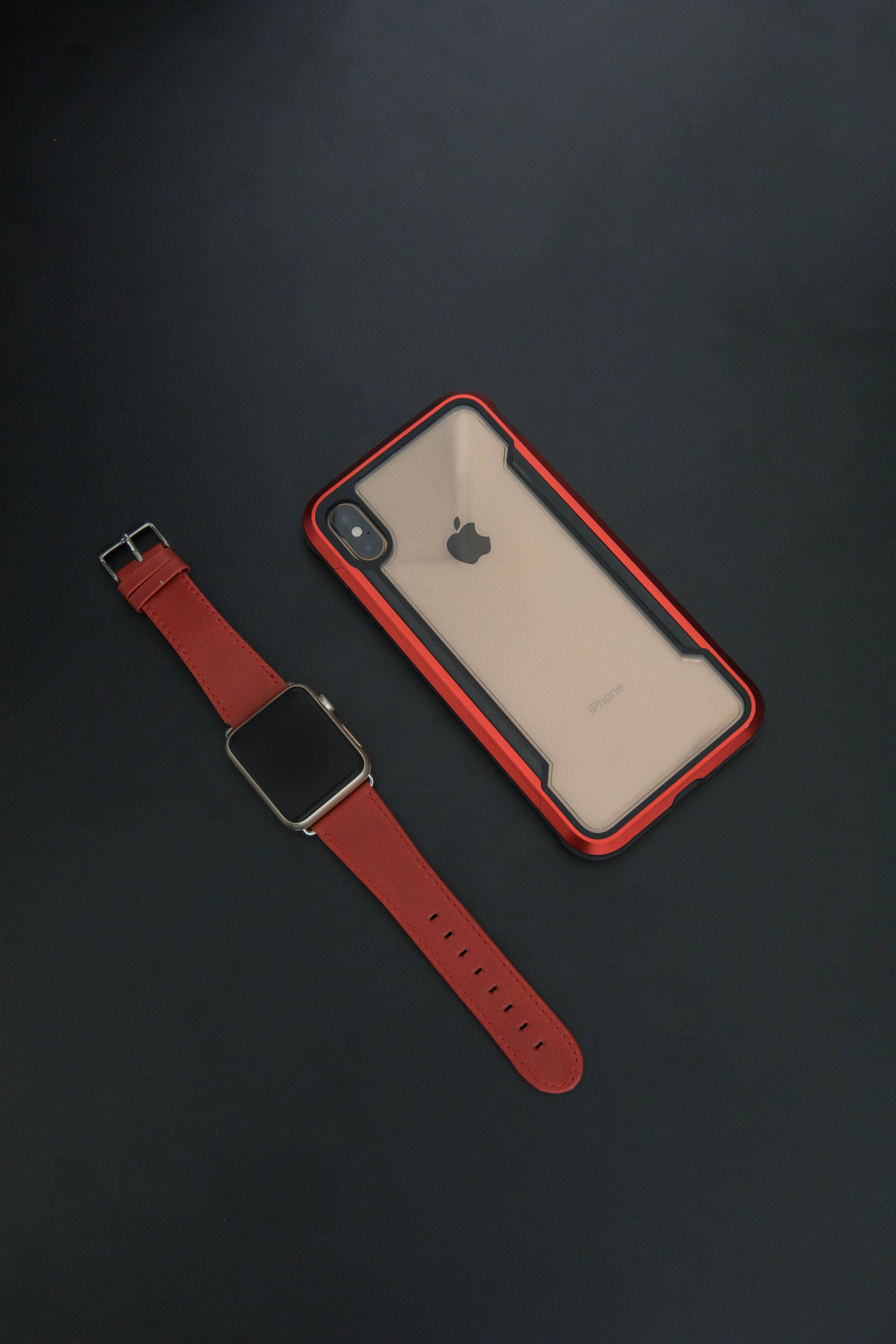 iPhone Xs Max 桌布 壁紙 — 紅色皮革 Apple Watch 和紅色邊框 iPhone 保護殼放在深色霧面表面上，呈現極簡產品照。