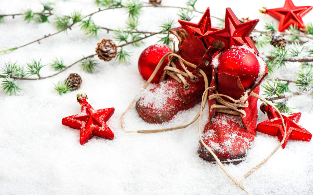 Red Christmas 桌布 壁紙 — 紅色節日靴子和裝飾品放在松樹枝和松果旁邊的新雪上。