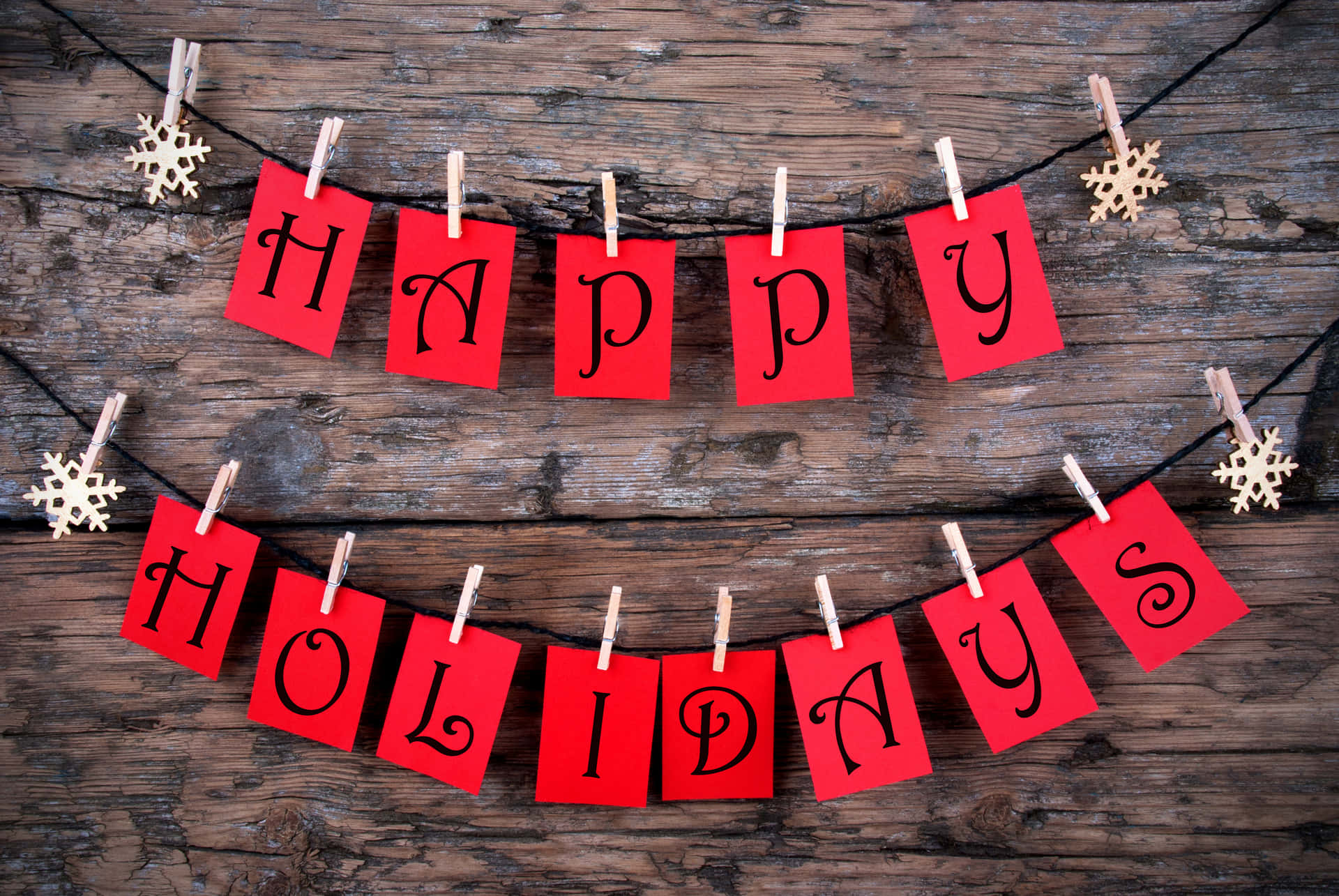 桌布 壁紙 — 紅色紙字母拼出 'HAPPY HOLIDAYS'，掛在黑色繩子上，用木衣夾和金色雪花裝飾，背景是鄉村風格的風化木頭。