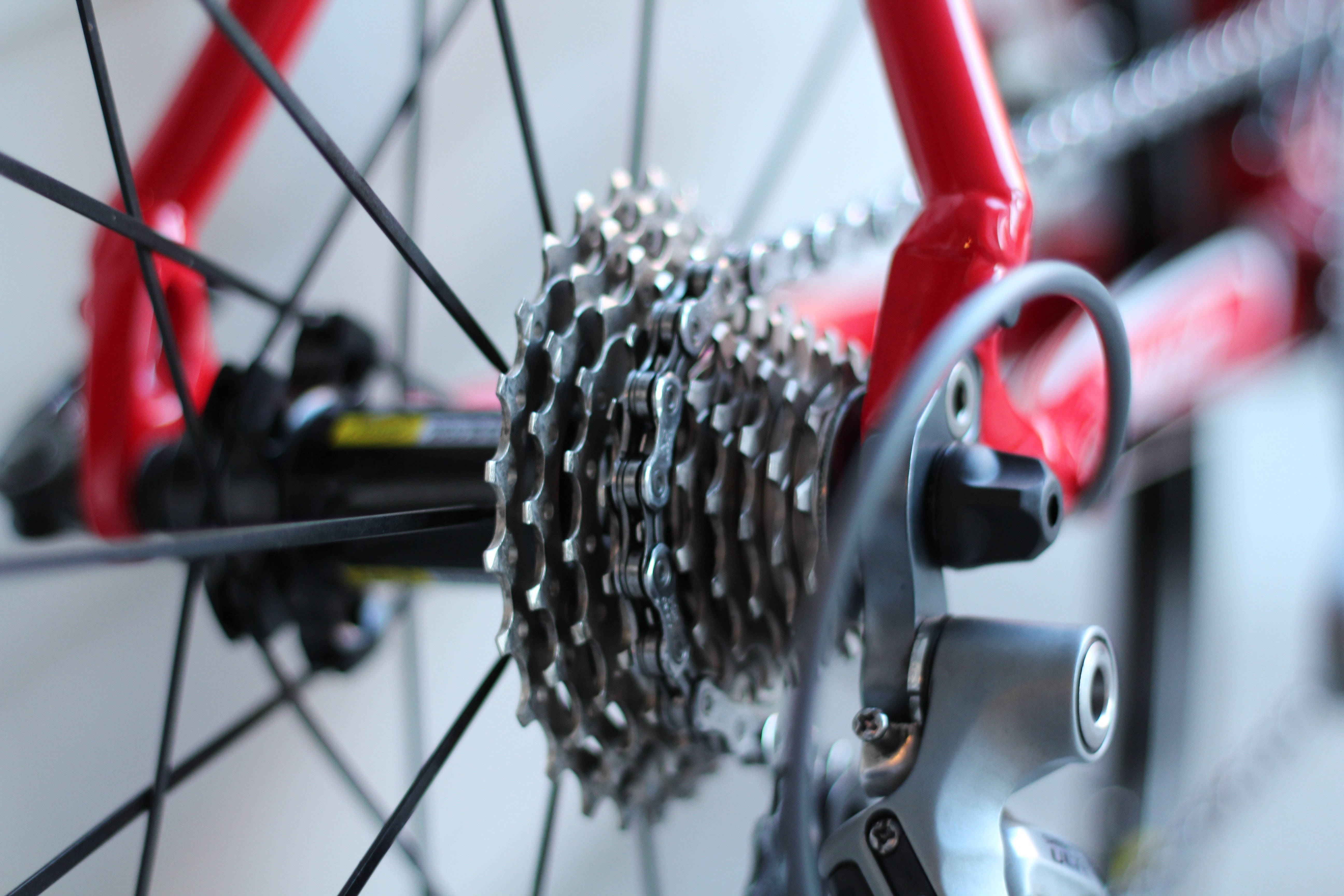 Bicycle 桌布 壁紙 — 紅色腳踏車的銀色齒輪卡式飛輪和後變速器的特寫，背景為模糊的白色。