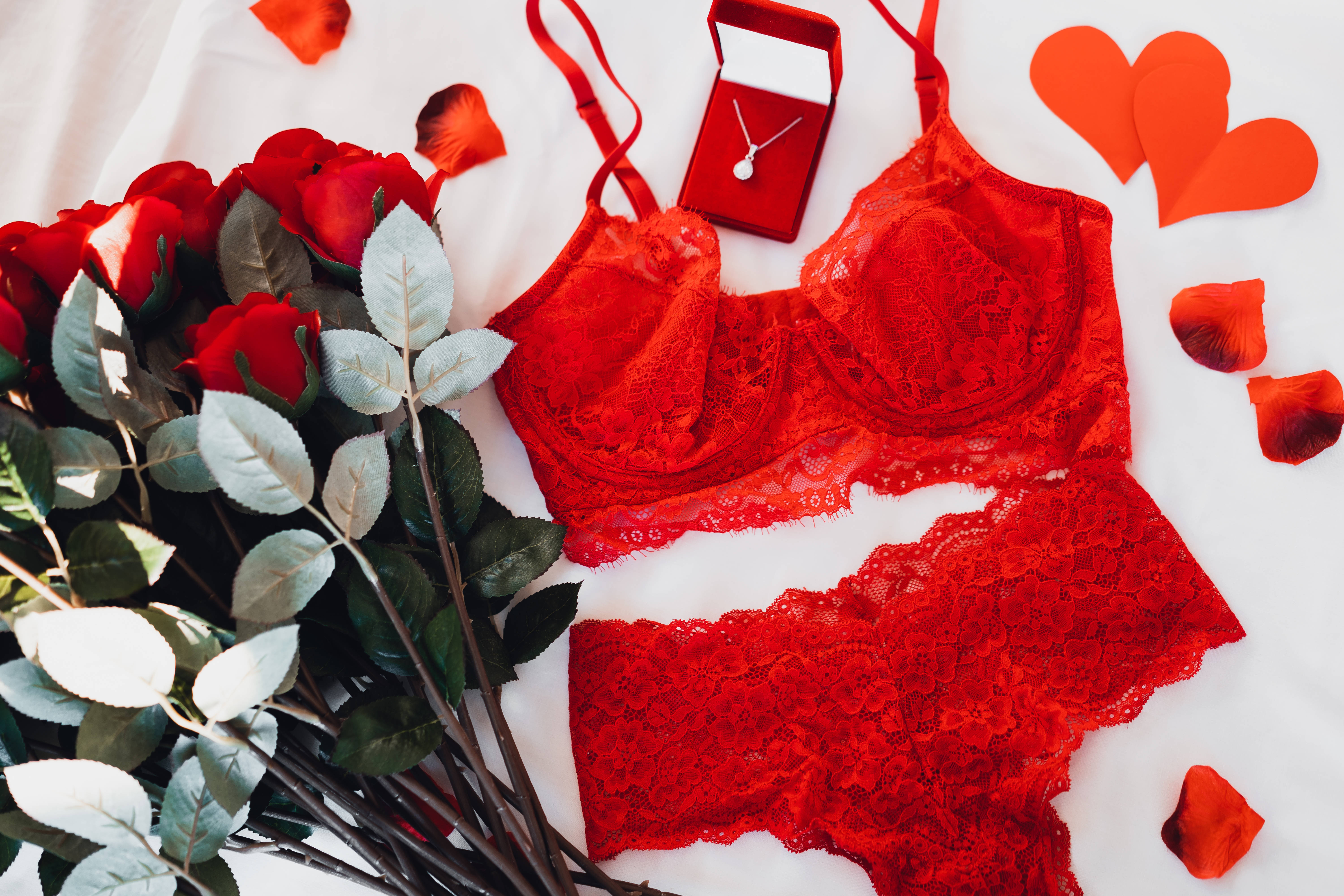 rose aesthetic phone 桌布 壁紙 — 紅色蕾絲內衣和玫瑰擺放在白色布料上，配有心形盒子和散落的花瓣。