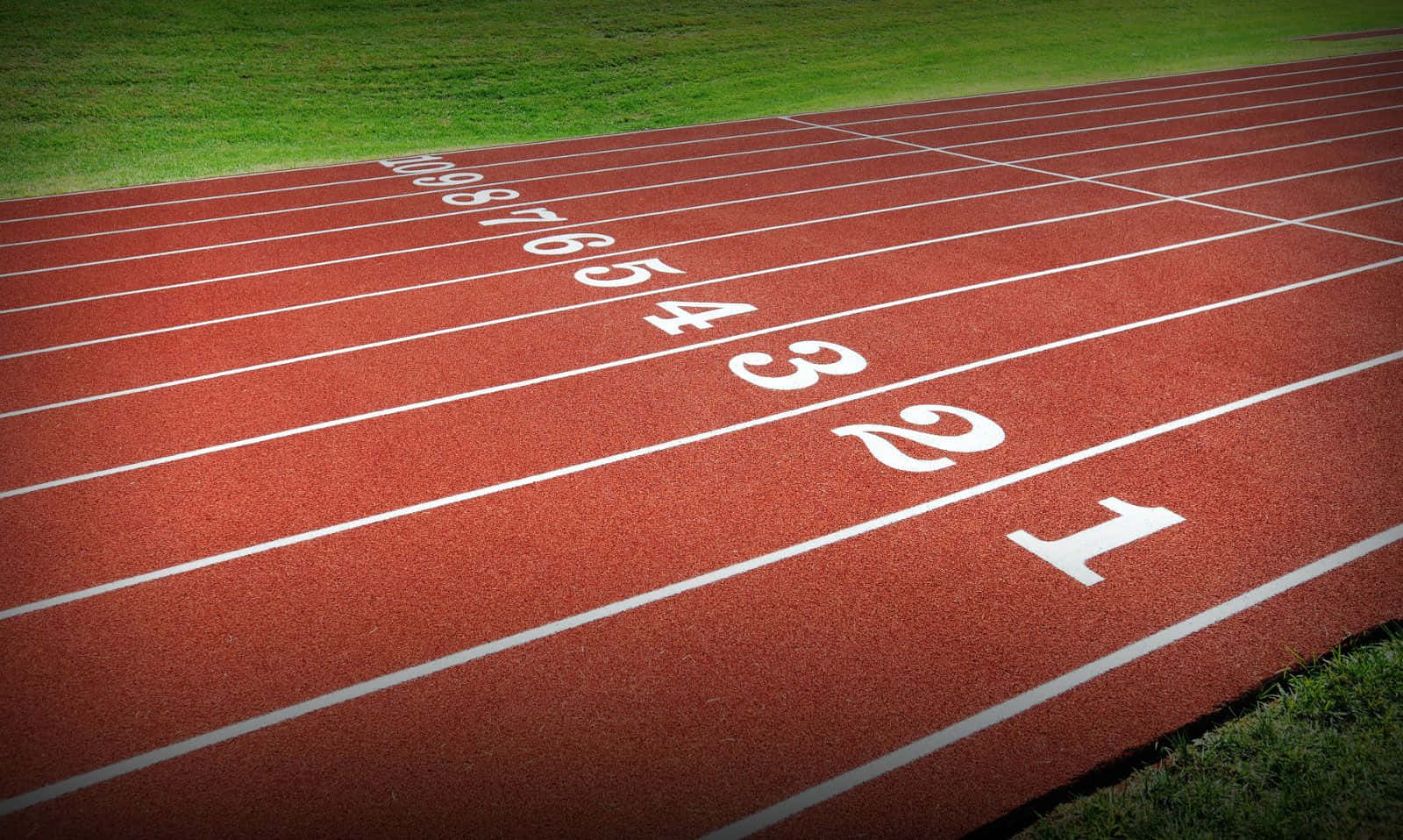 track 桌布 壁紙 — 紅色跑道的特寫視圖，有白色跑道號碼和綠色草地沿著彎道邊界。