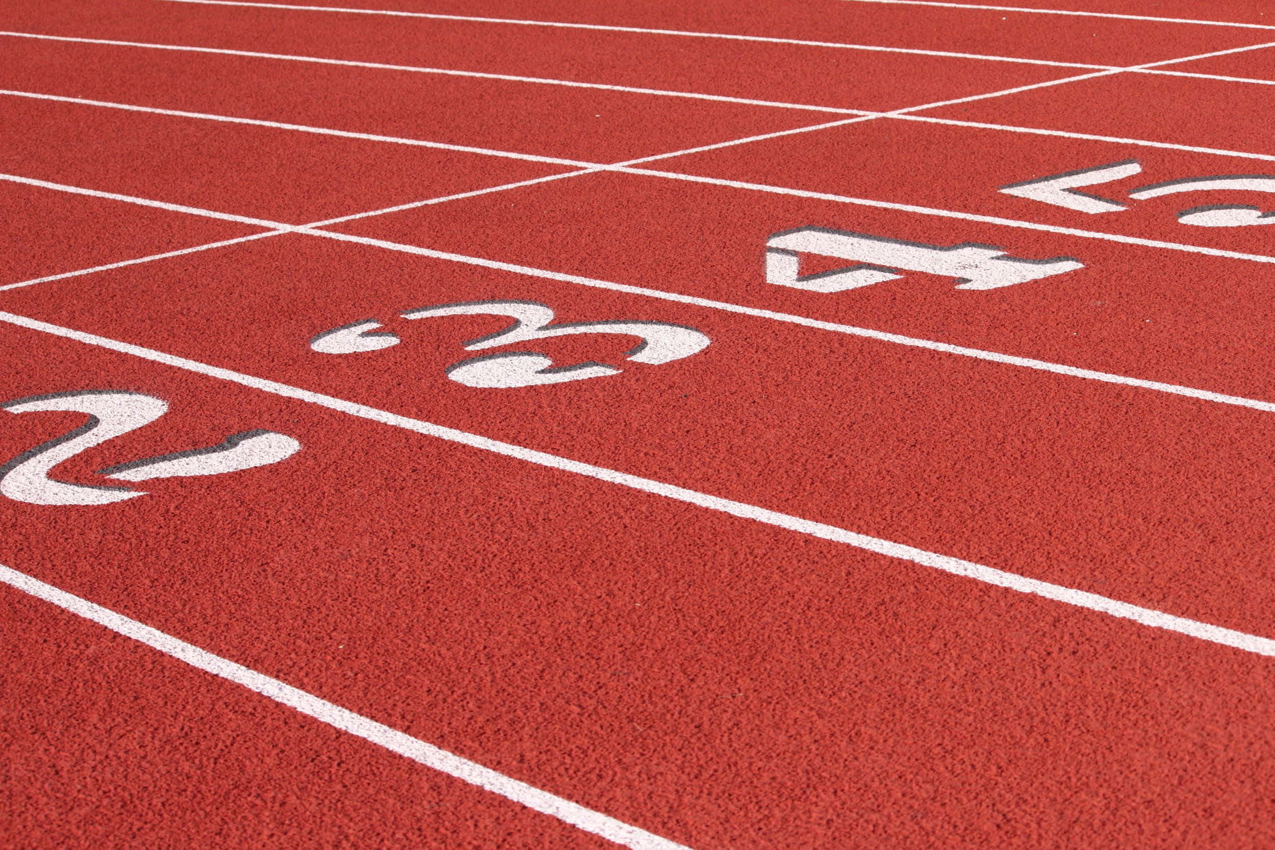 track 桌布 壁紙 — 紅色運動跑道近距離特寫，帶有白色賽道標記和編號賽道，展示紋理和透視效果。