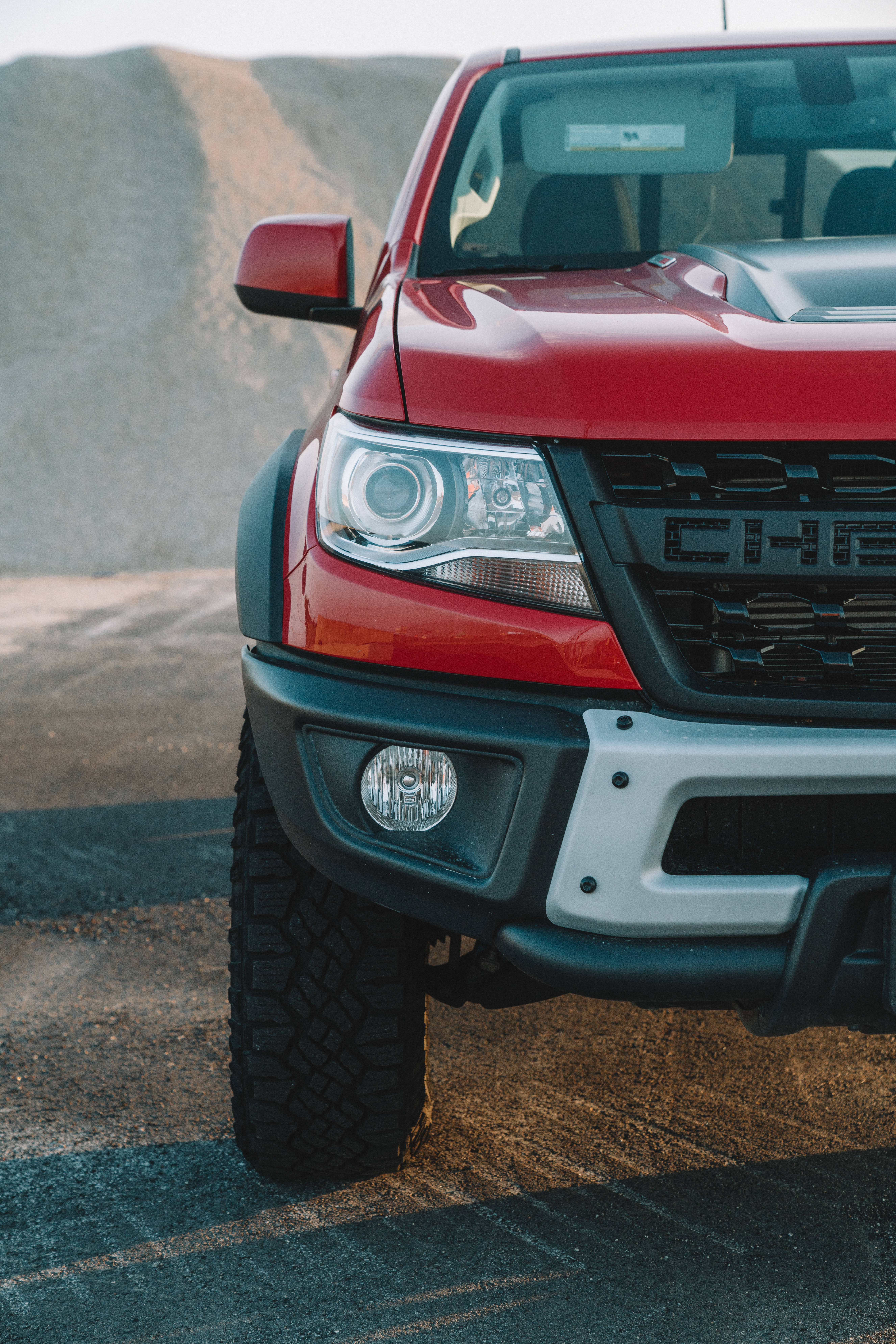 Chevrolet 桌布 壁紙 — 紅色雪佛蘭卡車堅固前端的特寫，停泊在塵土飛揚的道路上，背景有碎石山丘。