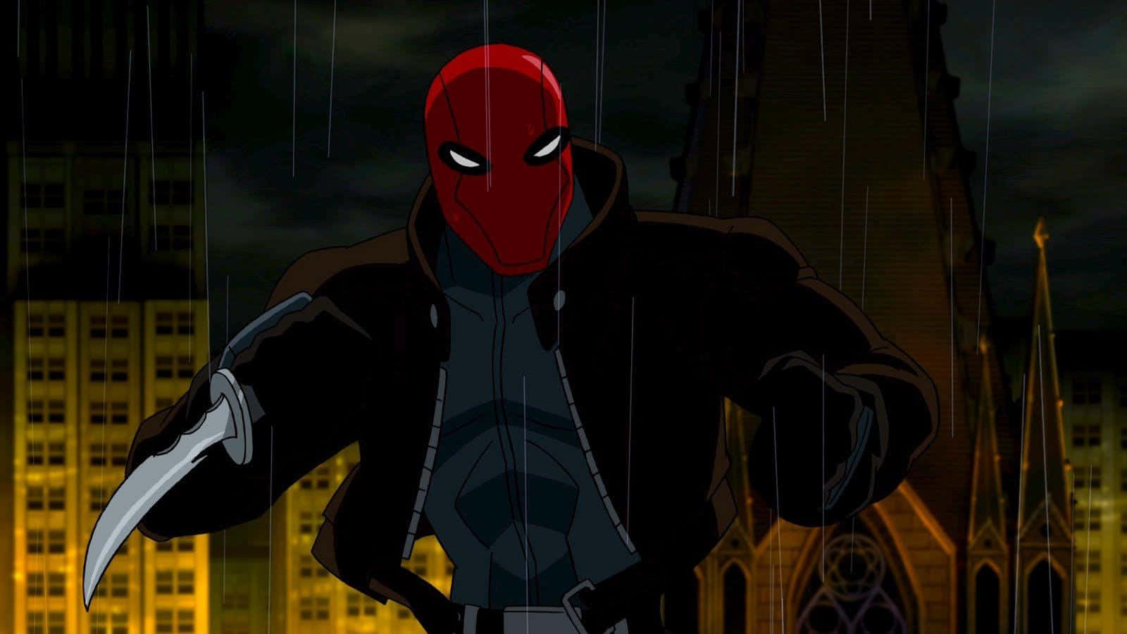 Batman Under The Red Hood 桌布 壁紙 — 紅色面具義警站在雨中，背景是城市天際線，有發光的窗戶和哥德式教堂尖塔。