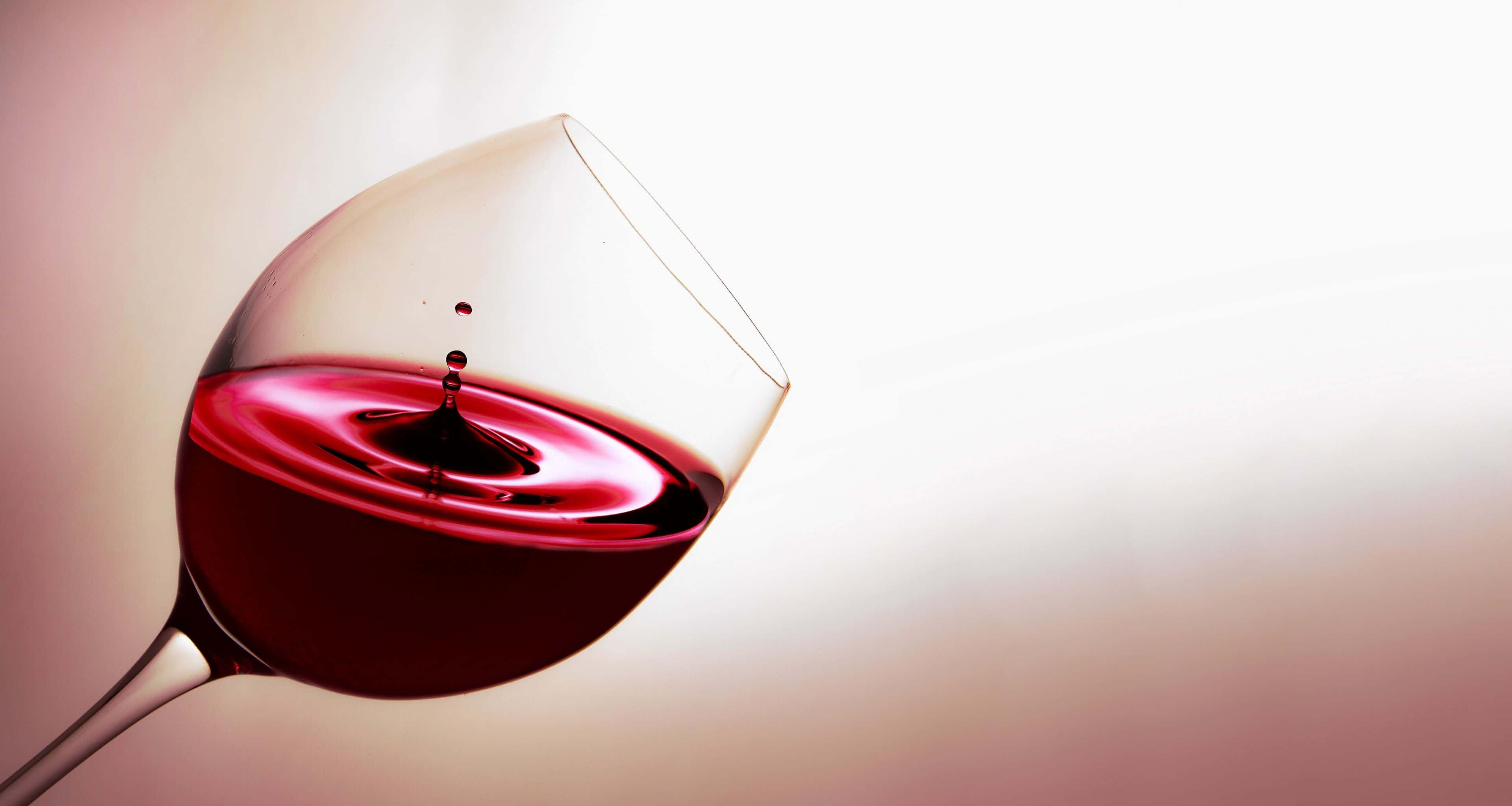 Red Wine Glass 桌布 壁紙 — 紅酒杯的特寫，紅酒在液體中形成完美漣漪，一滴酒濺入其中。