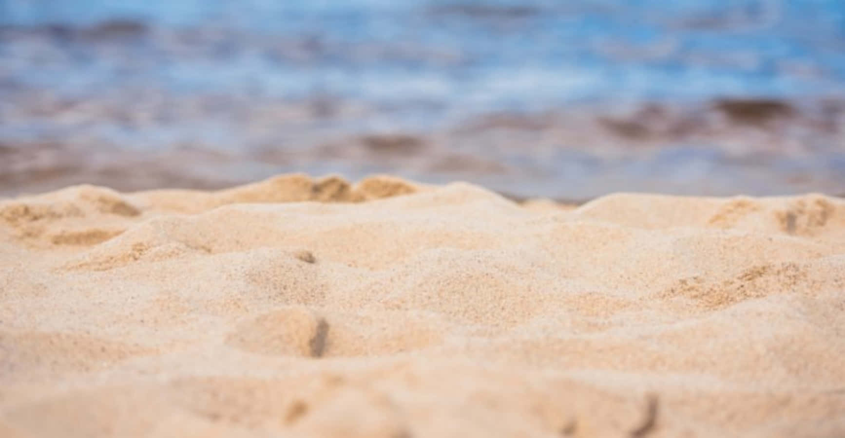 sand 桌布 壁紙 — 紋理金色沙灘的特寫，背景是模糊的藍色海浪。