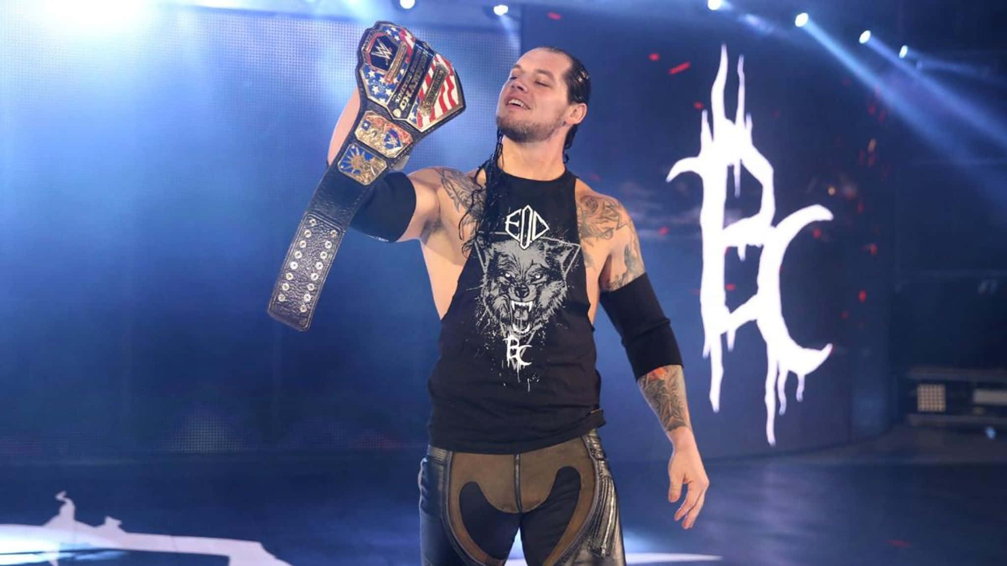 WWE 桌布 壁紙 — 紋身摔角手在明亮舞台燈光下高舉冠軍腰帶，背景有發光標誌。