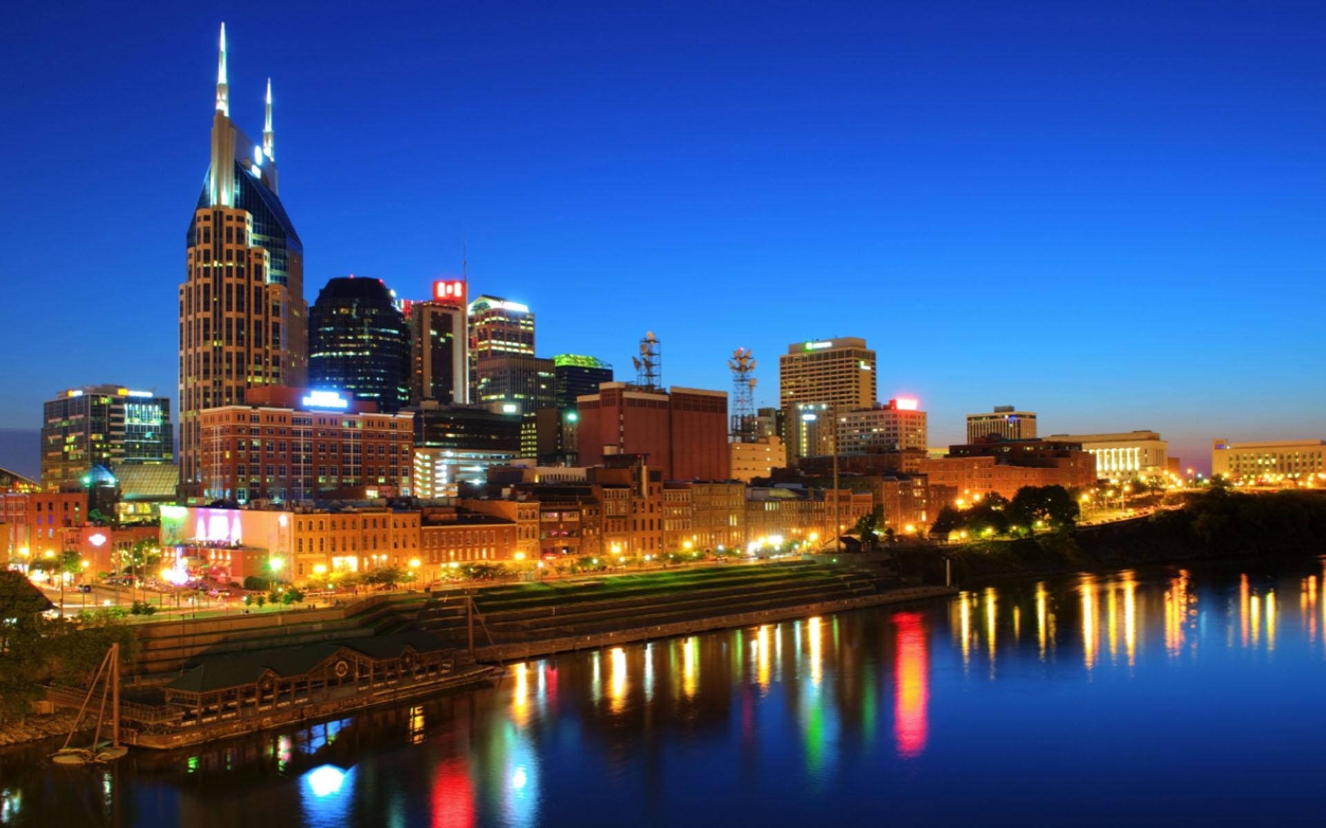 Tennessee 桌布 壁紙 — 納什維爾黃昏時分天際線，燈火通明的摩天大樓倒映在下方平靜的河流中。