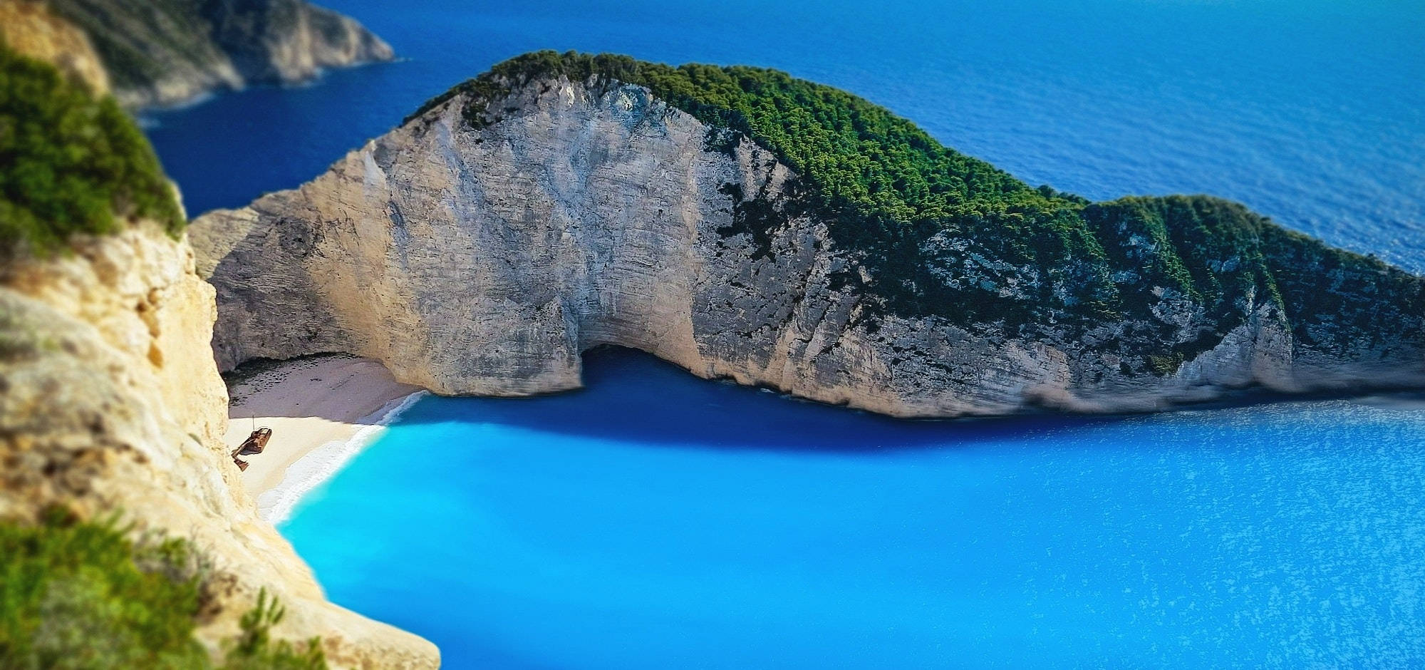 桌布 壁紙 — 納瓦吉奧海灘的壯麗景色，碧綠的海水被高聳的白色懸崖環抱，懸崖上覆蓋著茂密的綠植。