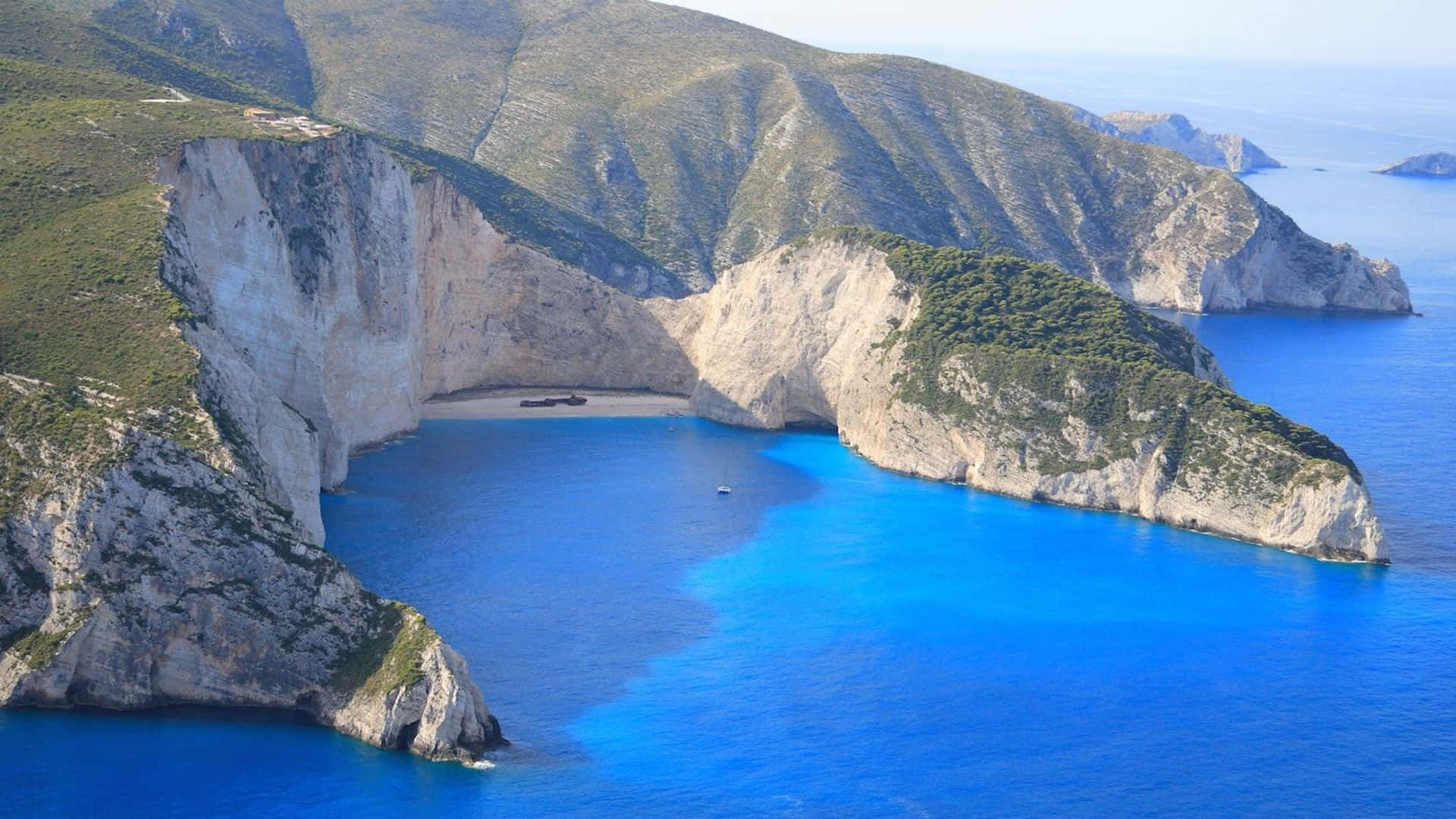 Greek Beach 桌布 壁紙 — 納瓦吉奧海灘的鳥瞰圖，碧綠的海水被陡峭的綠色懸崖環繞，岸邊有一艘沉船。