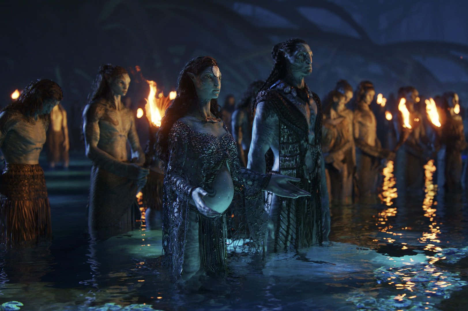 Avatar 2 The Way Of Water 桌布 壁紙 — 納美人站在發光的水中，在黑暗的樹冠下舉行神聖的夜間儀式，手持火炬。