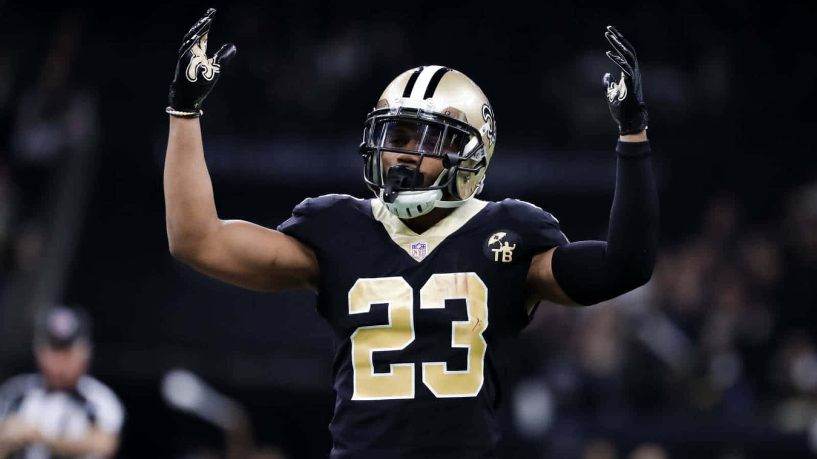 New Orleans Saints 桌布 壁紙 — 紐奧良聖徒隊的23號美式足球員在夜間比賽中，於球場燈光下高舉雙臂慶祝。