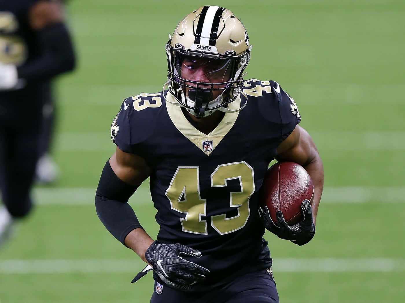 Marcus Williams 桌布 壁紙 — 紐奧良聖徒隊的美式足球員身穿黑金色制服，抱著球在綠色球場上衝刺。