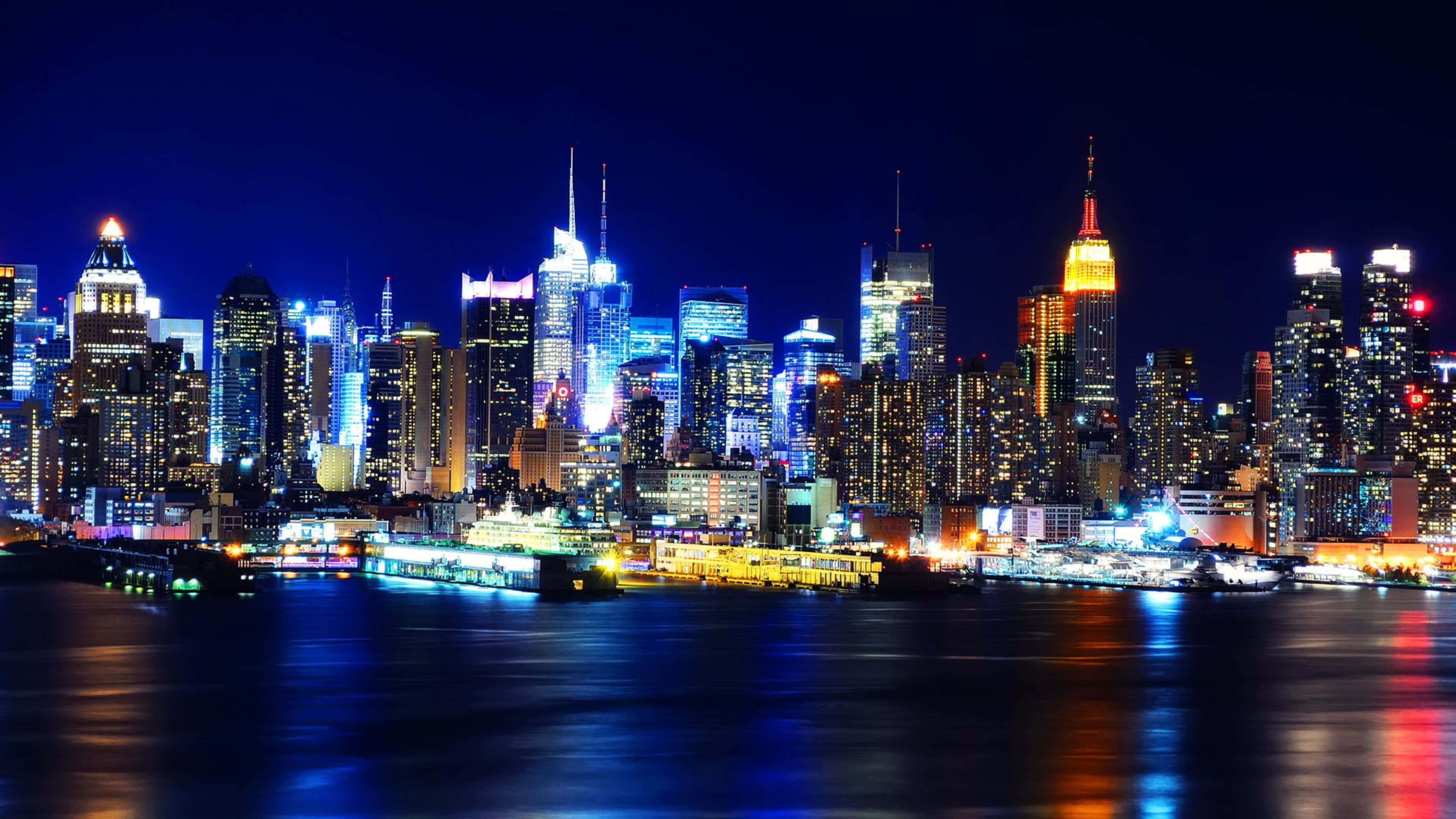 桌布 壁紙 — 紐約令人目眩的夜景，摩天大樓在深色水面上反射出藍色和金色的光芒。