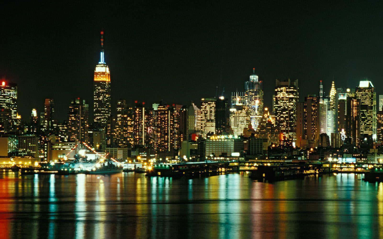 New York 桌布 壁紙 — 紐約令人目眩的夜景，摩天大樓在漆黑的天空中閃耀，它們的燈光倒映在下方平靜的水面上。