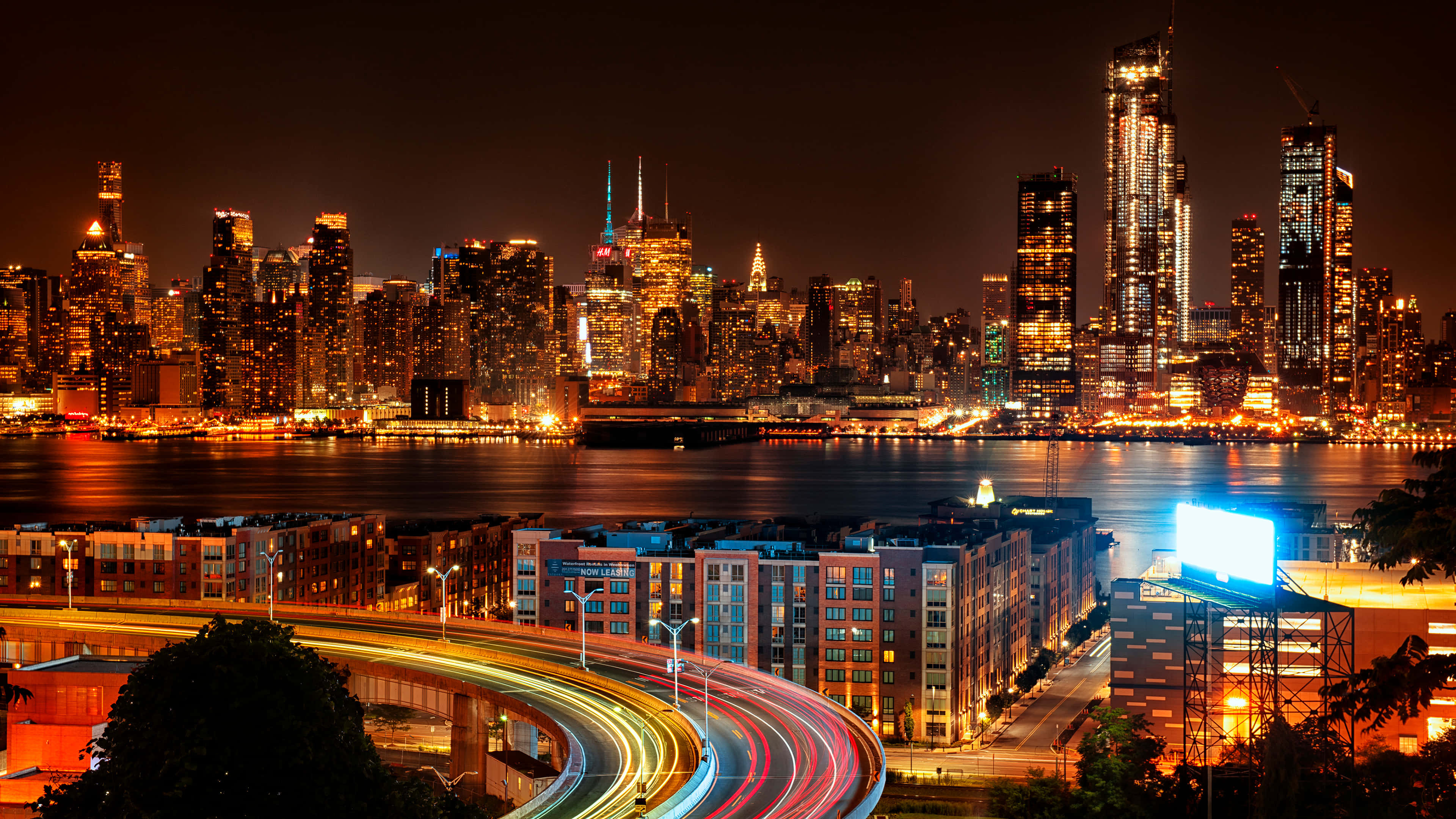City Night 桌布 壁紙 — 紐約令人目眩的夜景，閃爍的摩天大樓和彎曲高速公路上車流形成的鮮豔光軌。