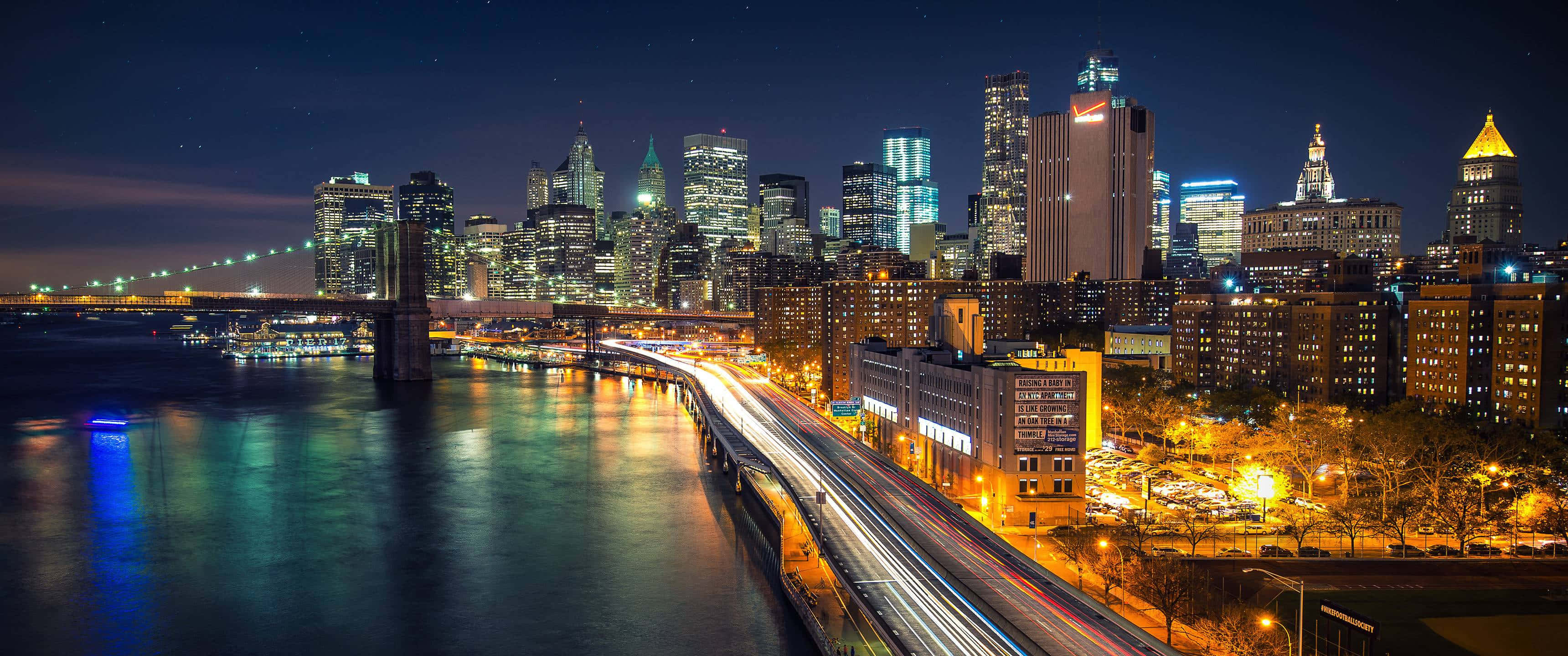 Brooklyn Bridge 桌布 壁紙 — 紐約令人眼花撩亂的夜景，閃爍的摩天大樓和水上橋樑上交通的光跡。