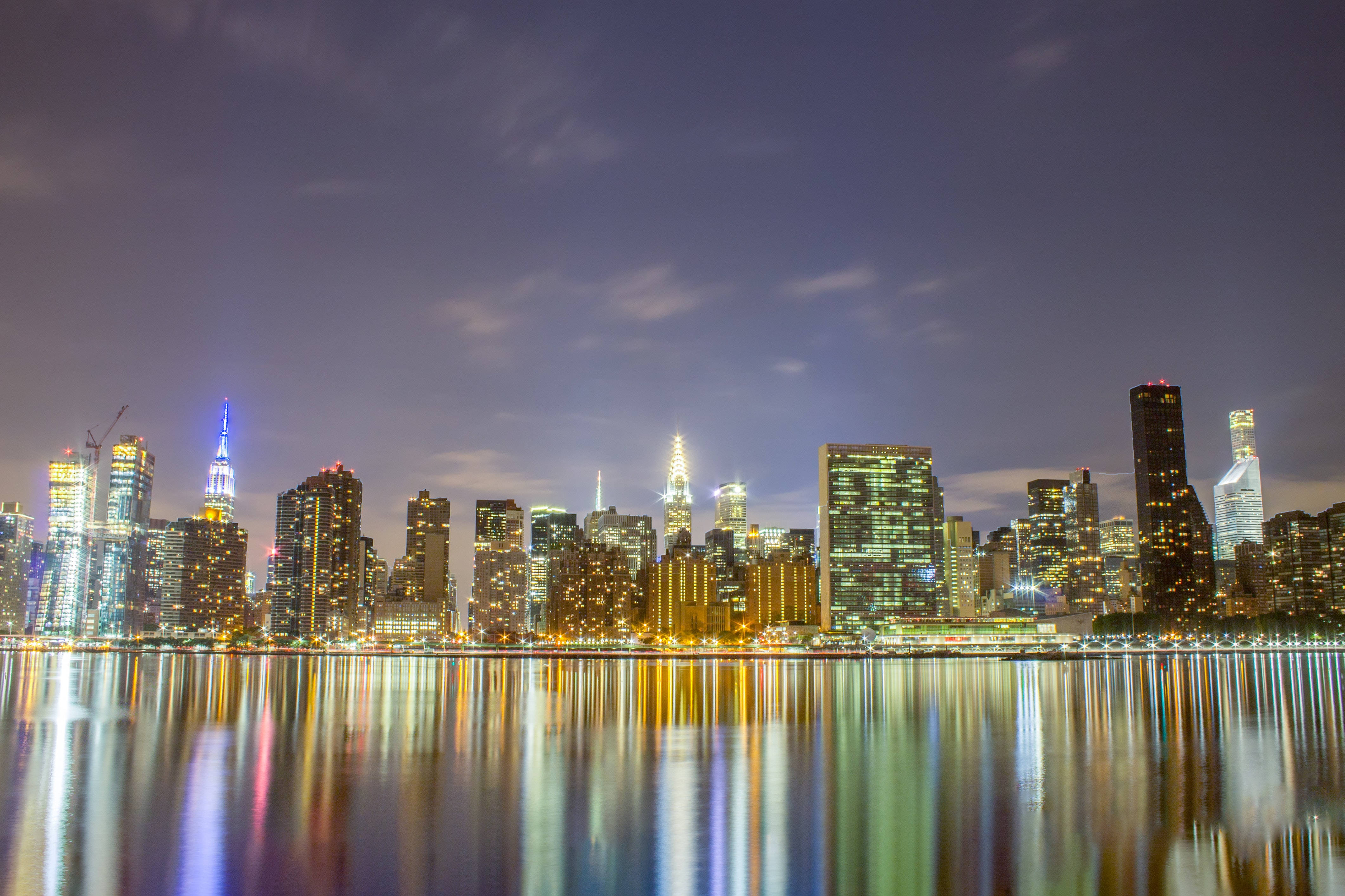 Nyc Aesthetic 桌布 壁紙 — 紐約令人驚嘆的夜景，摩天大樓在暮色蒼茫的天空中閃耀，它們的燈光完美地倒映在下方平靜的水面上。