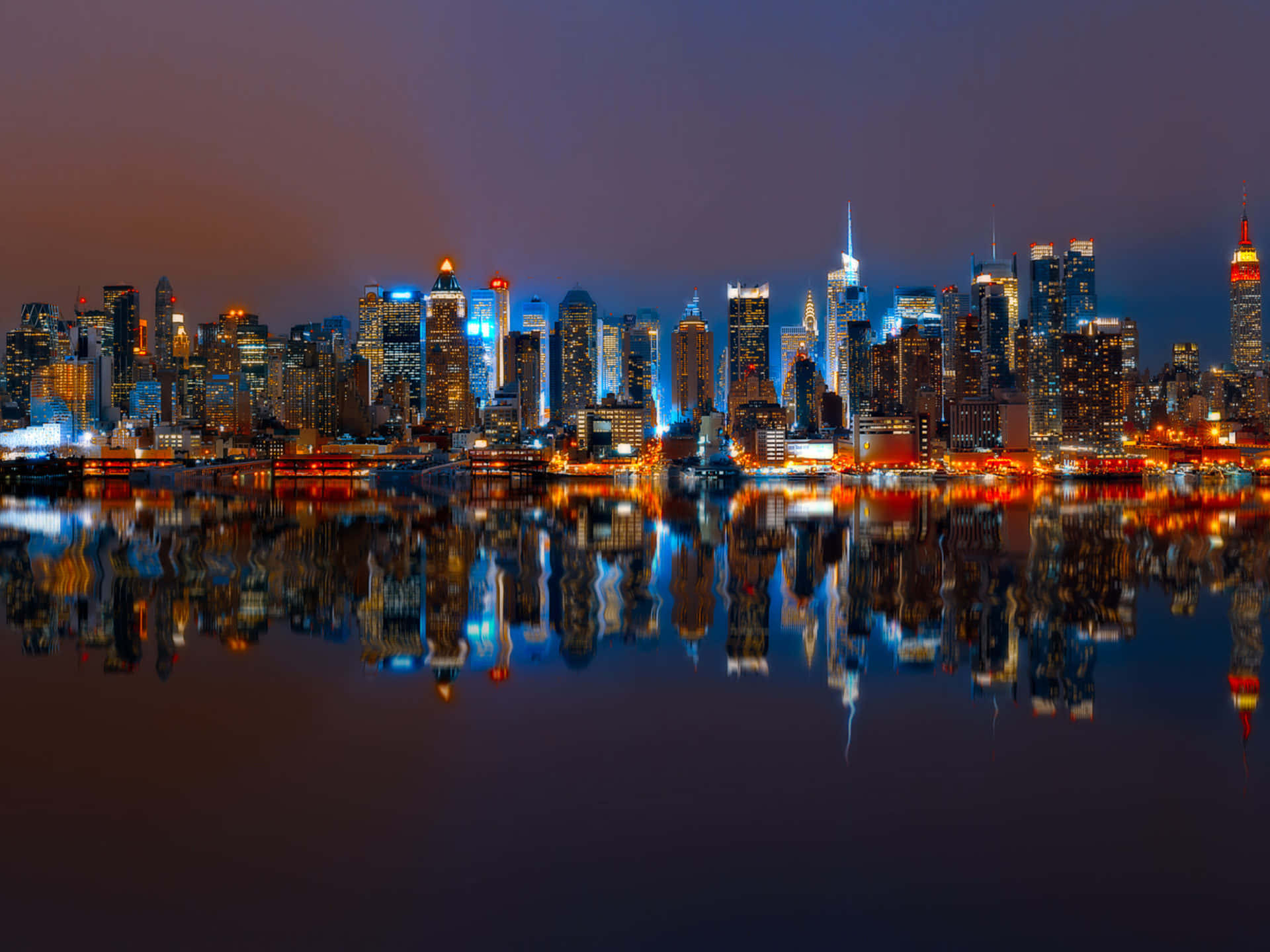 New York City Landscape 桌布 壁紙 — 紐約令人驚嘆的夜景，摩天大樓在藍色和橙色燈光中閃耀，完美倒映在平靜的水面上。