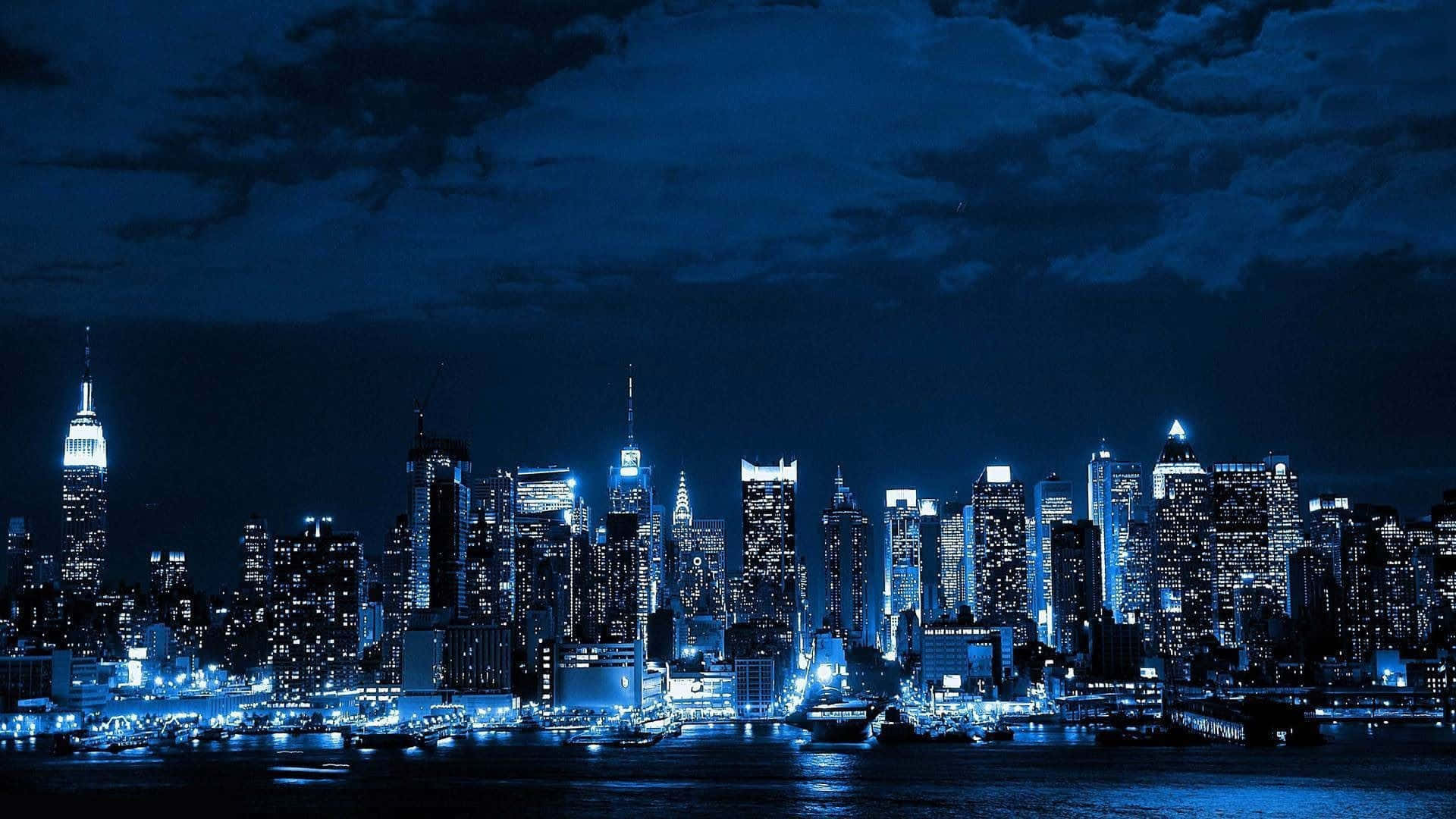 紐約市 桌布 壁紙 — 紐約令人驚嘆的夜景，摩天大樓在黑暗的水面上閃耀，映照在憂鬱的藍天下。