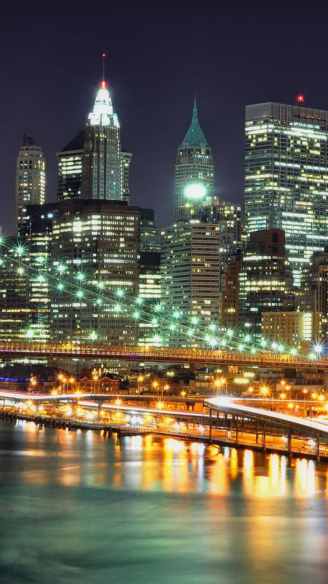 new york city iPhone x 桌布 壁紙 — 紐約令人驚嘆的夜景，摩天大樓燈火通明，發光的橋樑倒映在平靜的水面上。