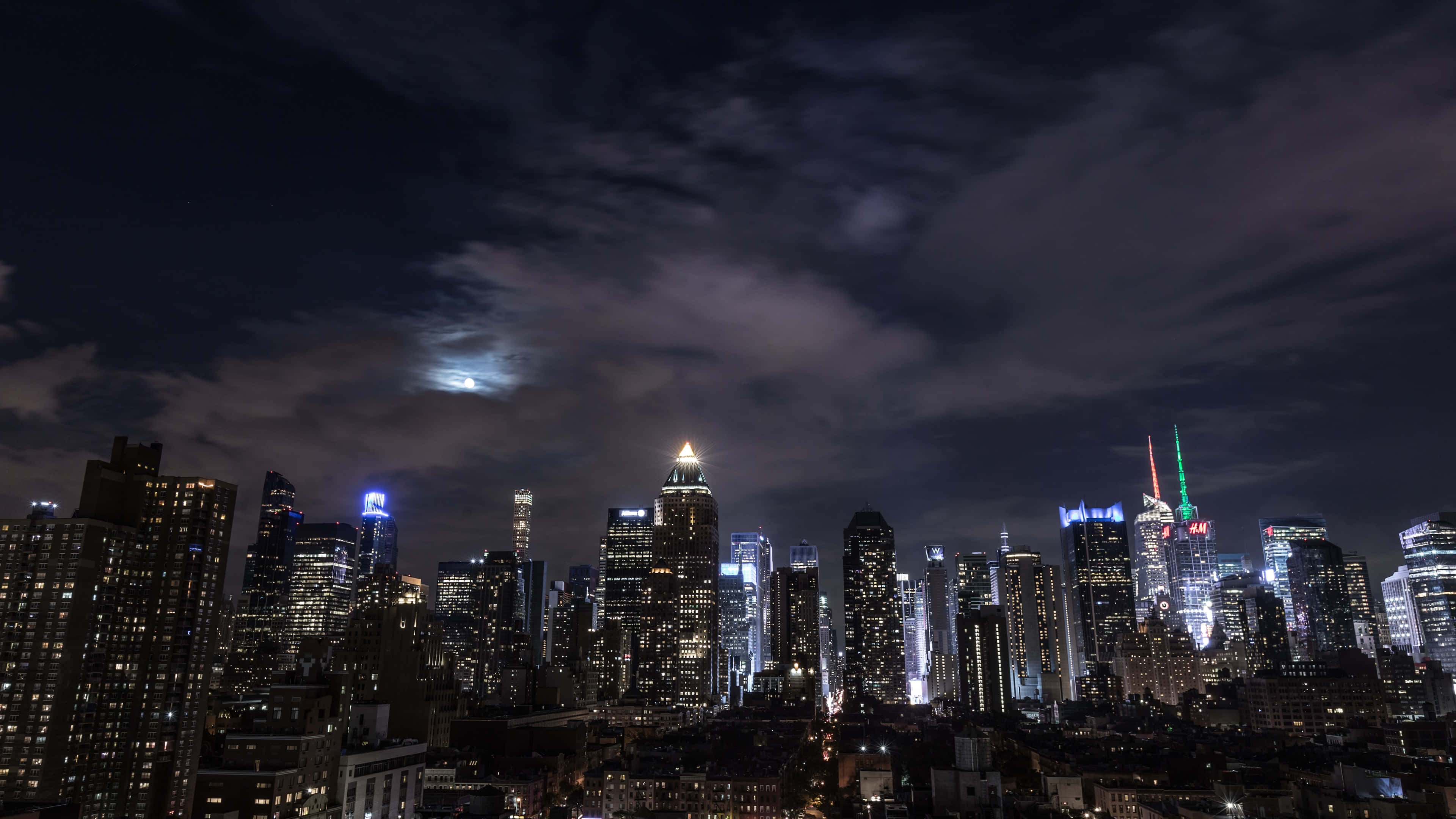 桌布 壁紙 — 紐約充滿活力的夜景，閃爍的摩天大樓和戲劇性雲層後明亮的月亮。